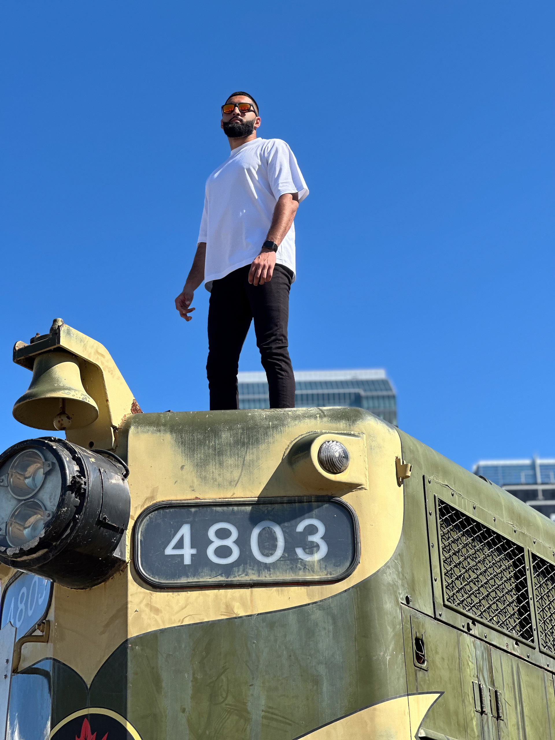 Muhammad Abbasi | Lifestyle | White oversized t-shirt, black jeans, colorful sneakers, standing on vintage train engine numbered 4803