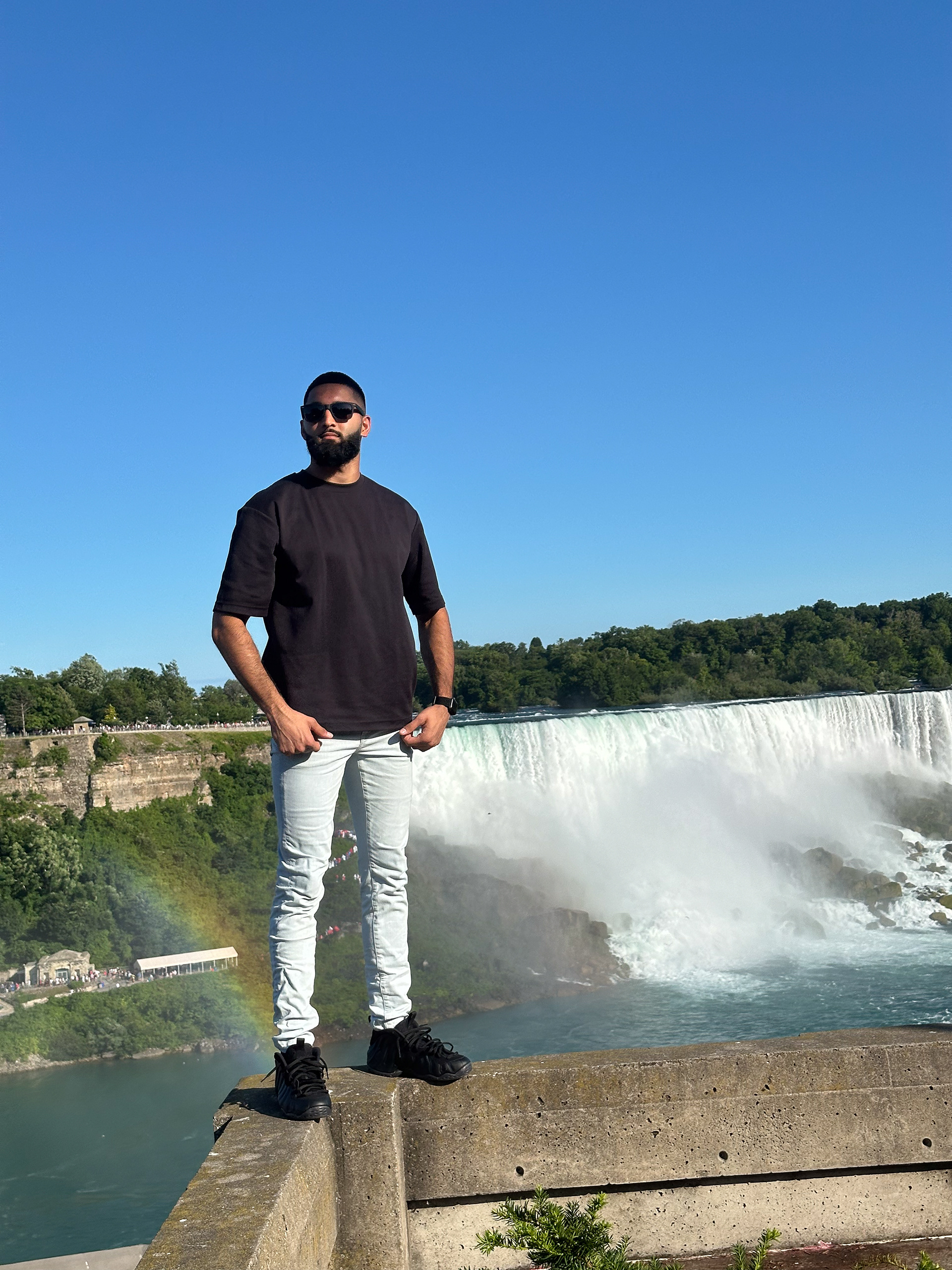 Muhammad Abbasi | Lifestyle | Black t-shirt, light blue jeans, black sneakers, front-facing pose near Niagara Falls