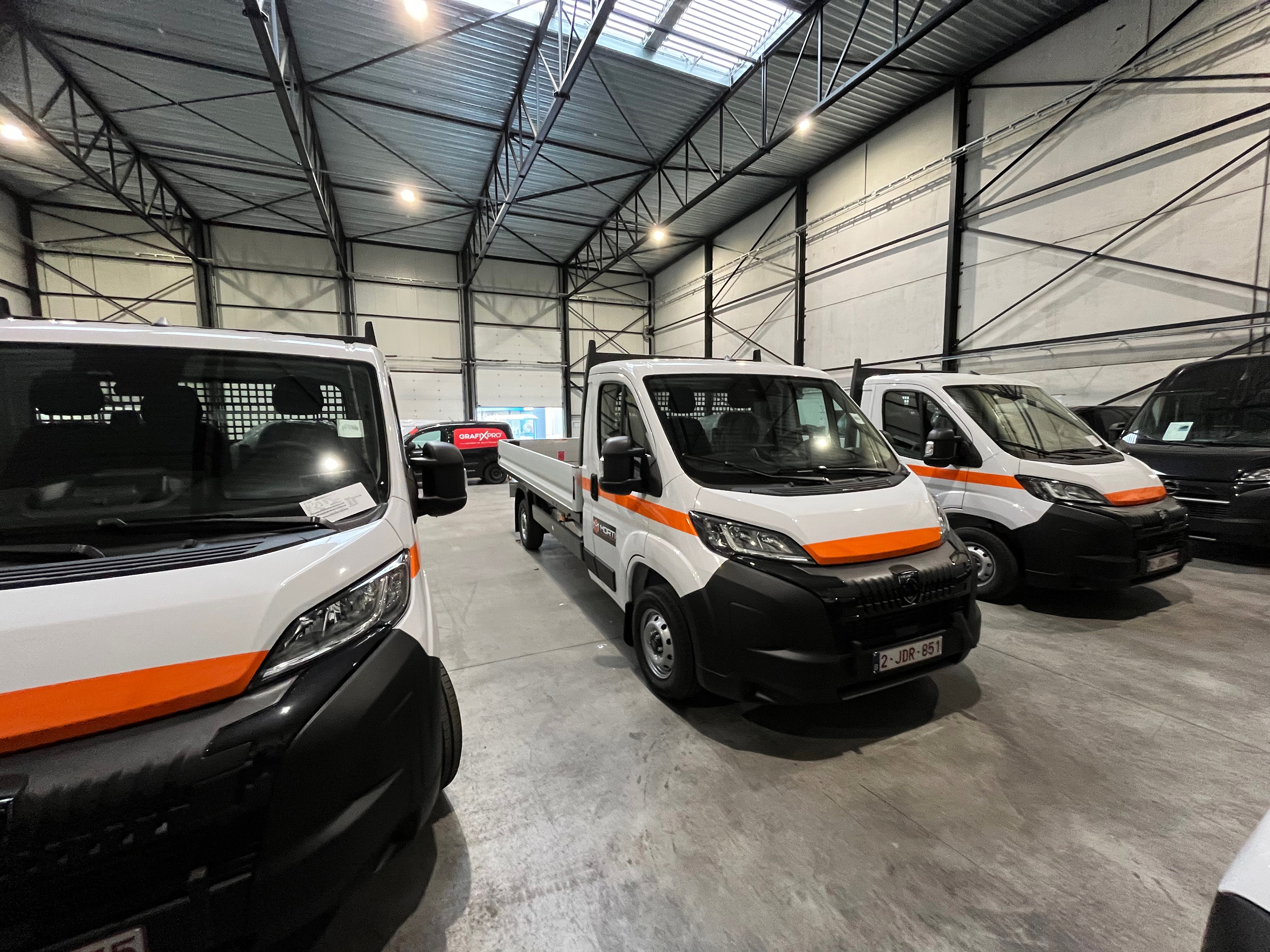 8 nieuwe bedrijfswagens met open laadbak voor Morti uit Drongen, strak uitgelijnd op de site van Traxxion te Evergem.