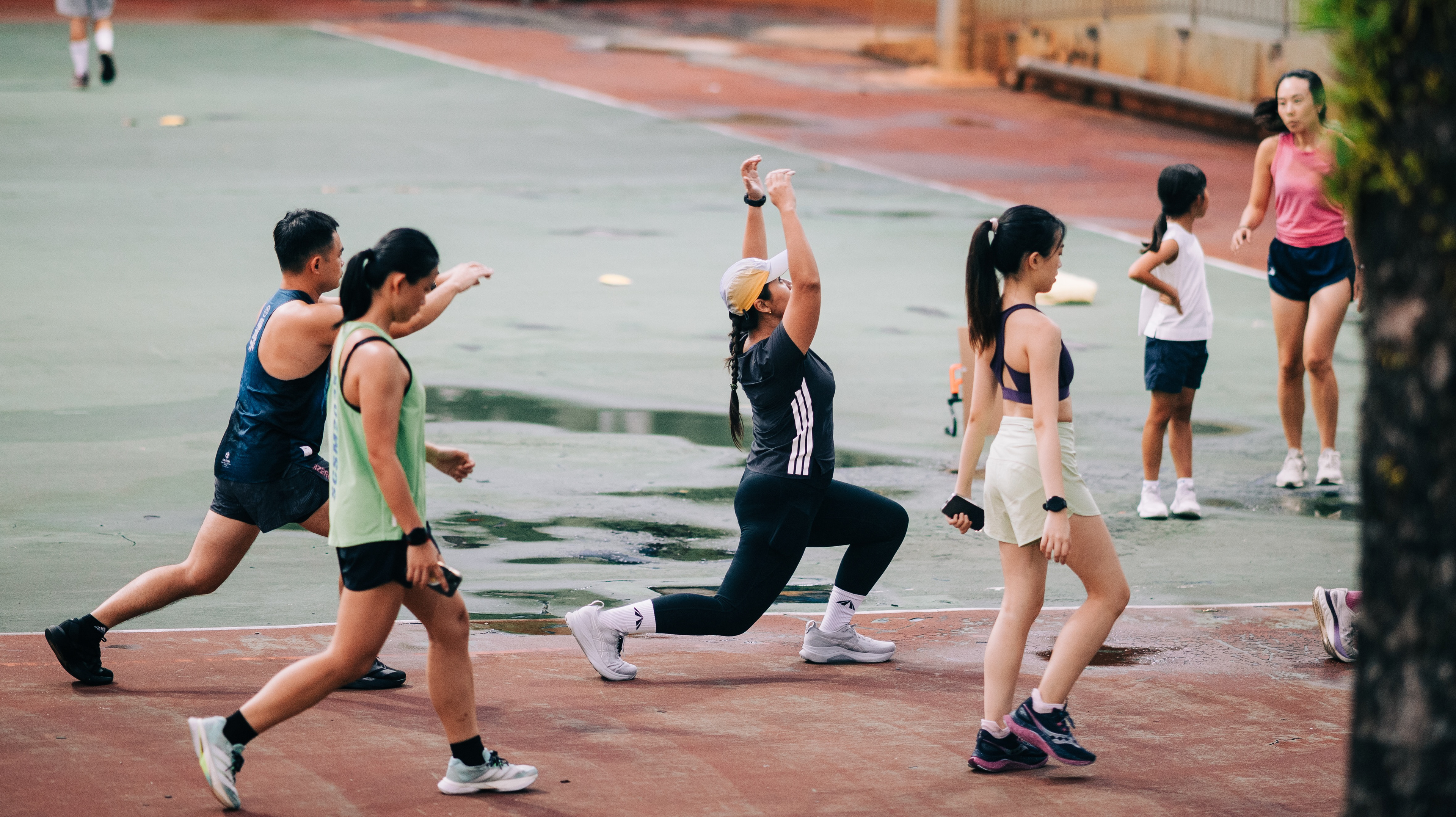 Atmospheric candid of an athletic community gathering in low blue light before a workout, captured from a distance as a quiet observer.