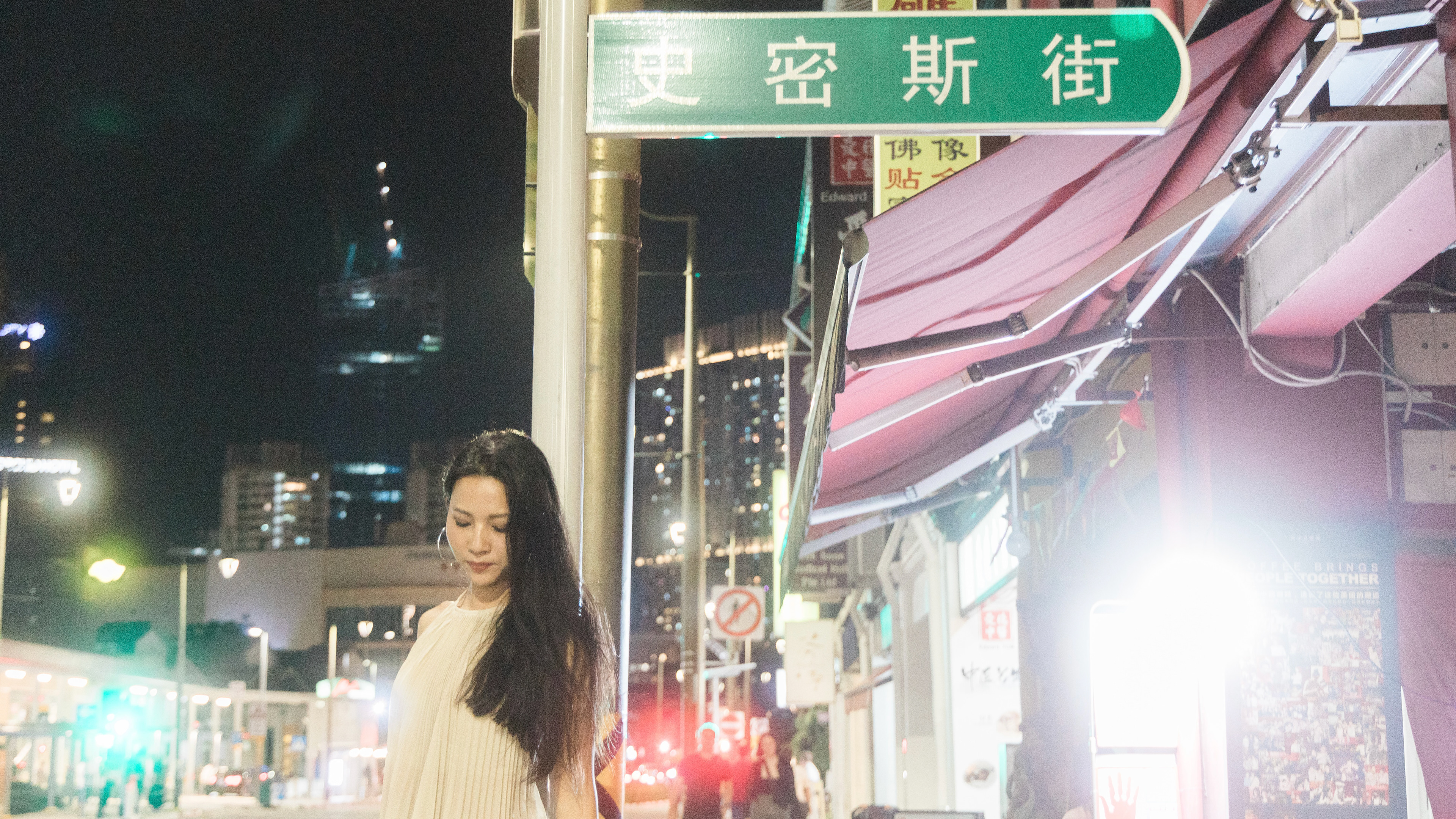 cinematic 16:9 night portrait of a woman walking past a heritage street sign on Smith Street, Singapore. The frame features atmospheric light bloom, traditional architectural textures, and a moody, low-key color palette.
