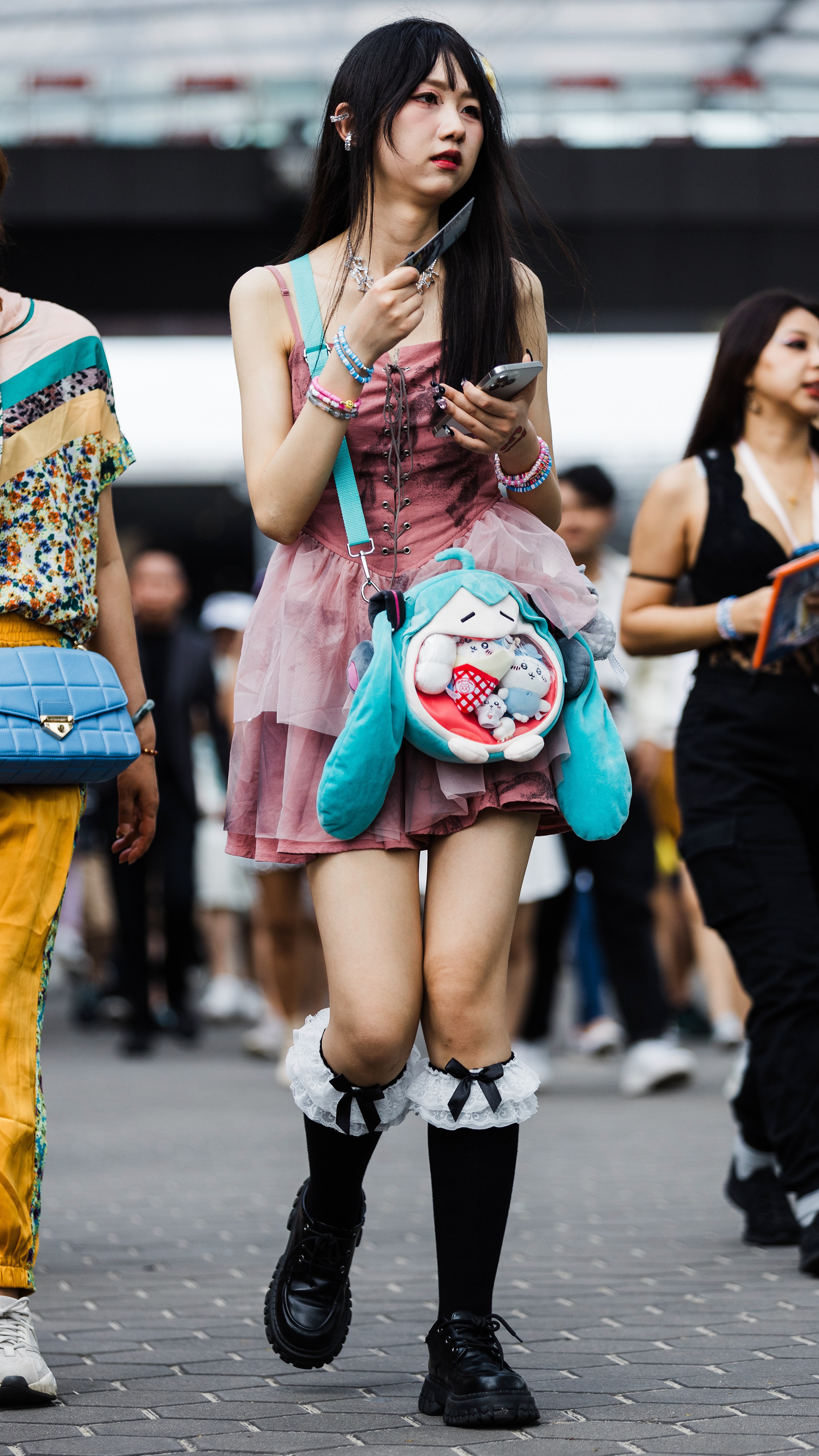 A study in stark geometry and persona extraction. An individual in dark, structured Eras Tour fashion, isolated through cinematic voyeurism within the city's labyrinthine transit areas. Texture and hard light focus.