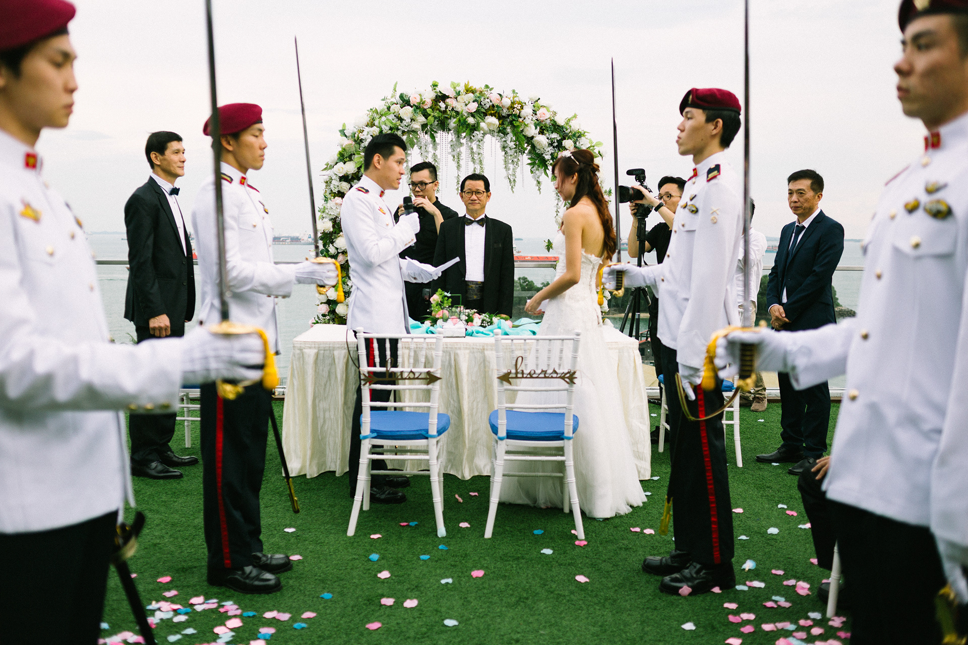 Cinematic high-fidelity documentation of a formal outdoor wedding ceremony featuring a military saber arch; wide-angle unit-still capturing ritual precision, structured symmetry, and candid human narrative in Singapore.