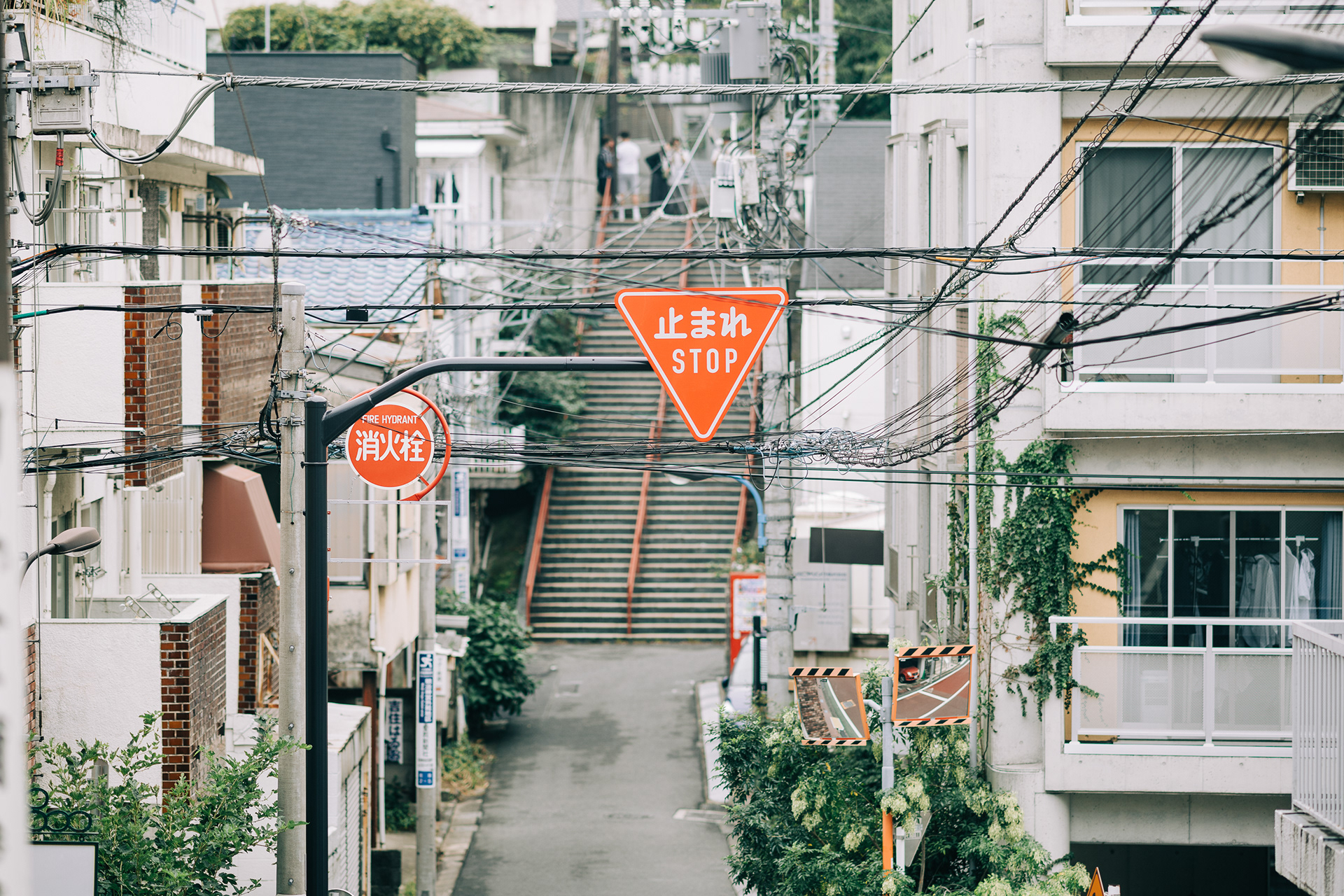 Atmospheric Tokyo street scene featuring a dense grid of overhead power lines and red Japanese road signs against a melancholic, overcast sky.