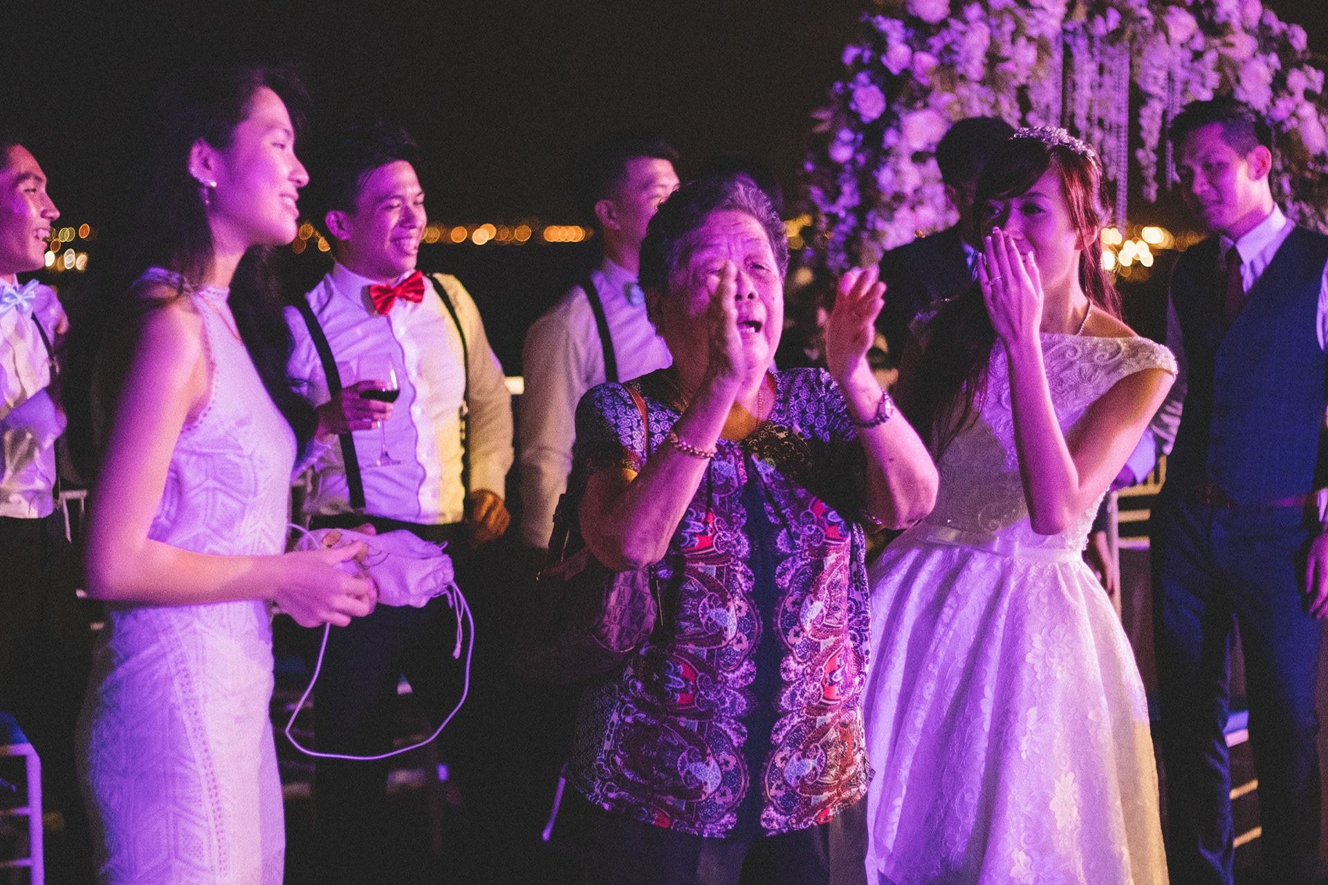 Cinematic high-fidelity extraction capturing raw emotional intensity and candid human expression during a nighttime urban celebration; low-light unit-still with vivid violet and amber luminescence.