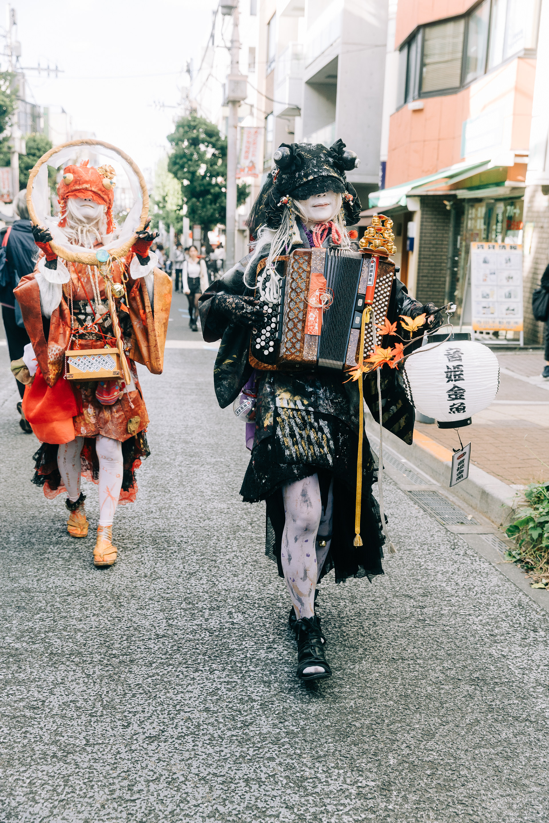 Cinematic street photography of performers in intricate, avant-garde costumes walking through a Tokyo neighborhood. High-detail textures and a shallow depth of field.