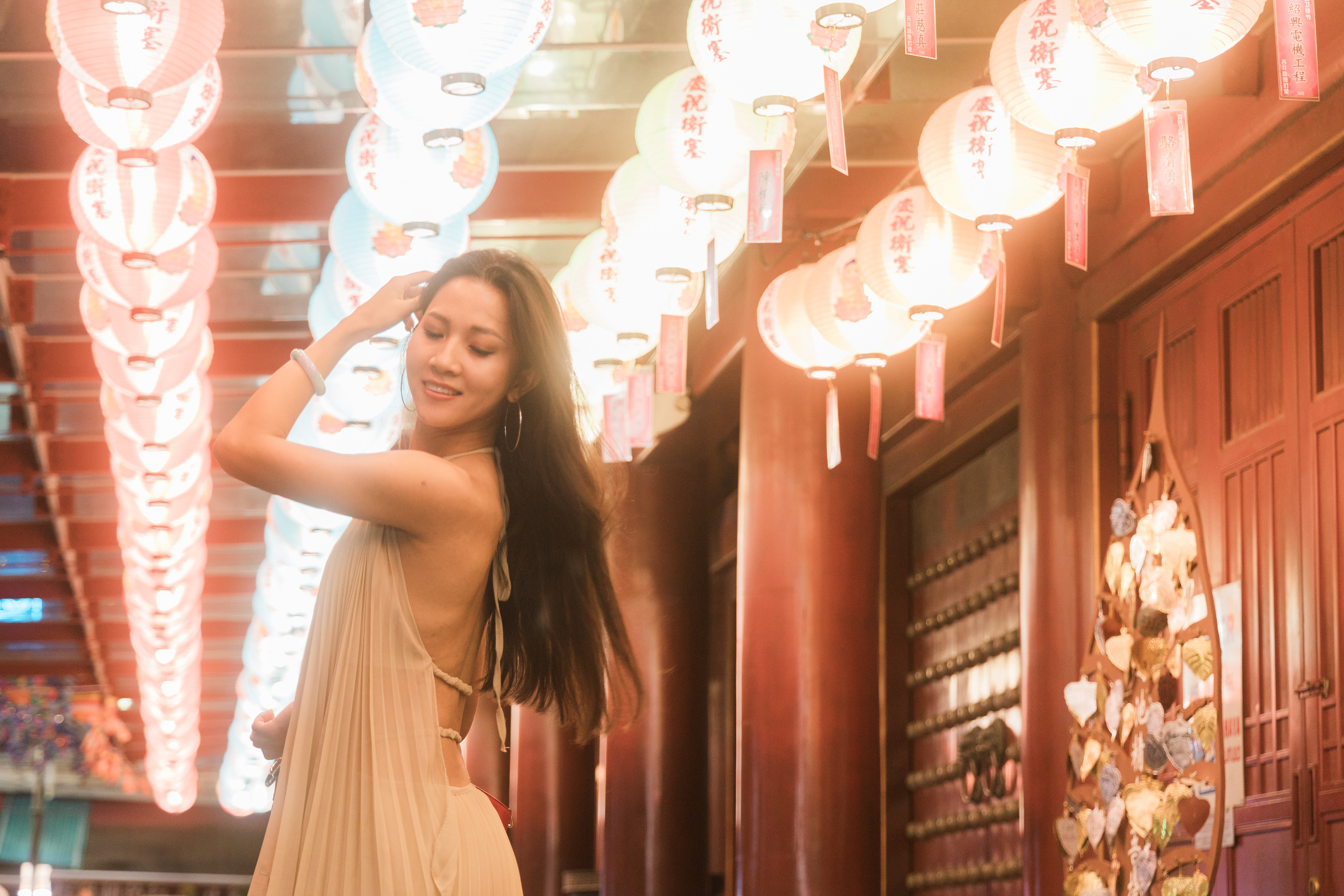 A warm, cinematic 16:9 portrait of a woman amidst a row of glowing traditional lanterns. The shot features heavy atmospheric bloom, soft lighting, and deep wooden textures, creating a dream-like urban narrative.