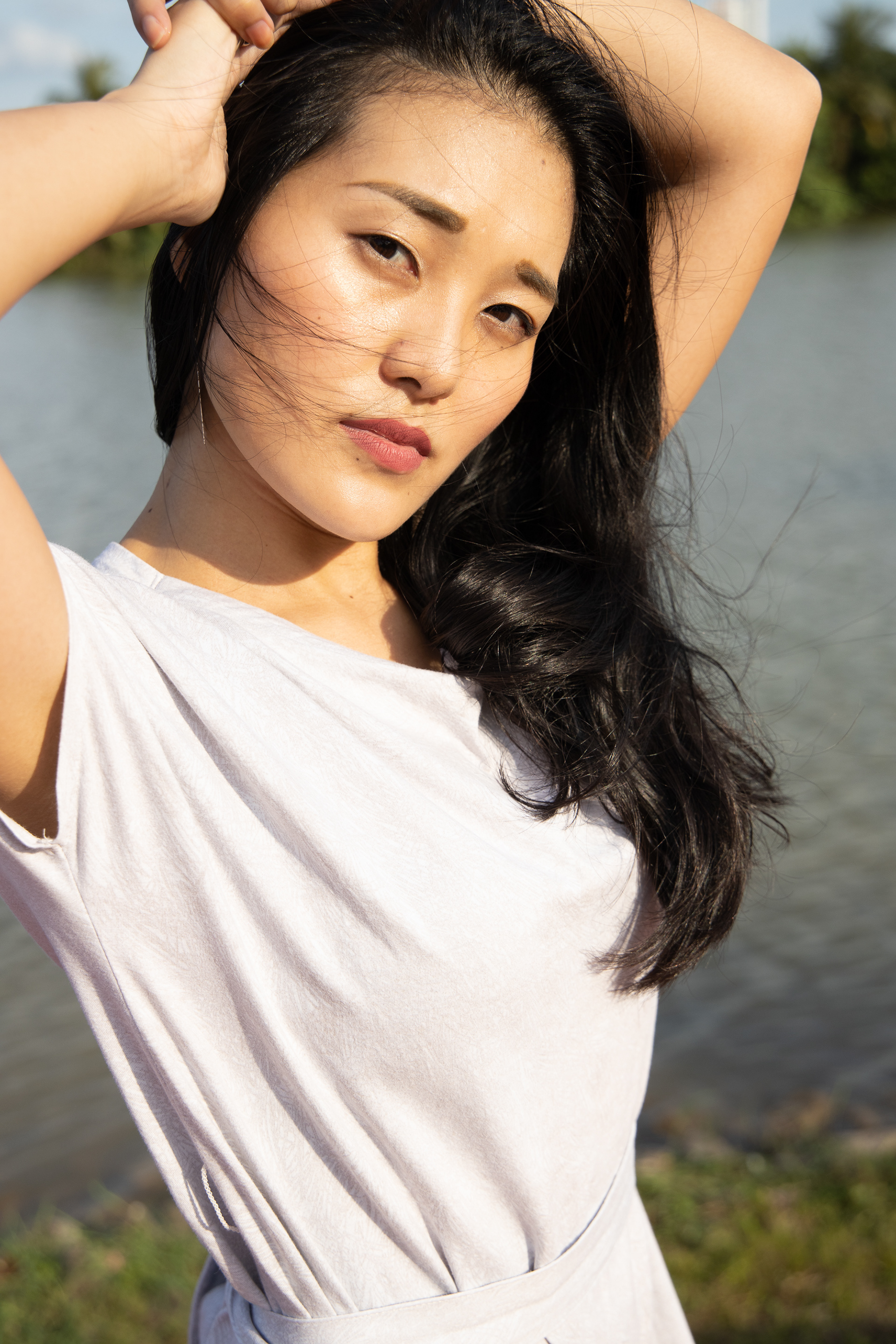 Cinematic unit-still portrait of a woman by the water; high-fidelity capture of natural afternoon light, wind-swept hair, and candid expression, emphasizing the individual within a serene environmental narrative.
