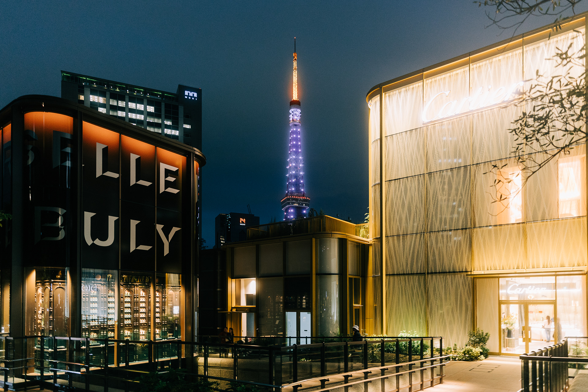 Symmetrical night photography of the Cartier building in Ginza with the Tokyo Tower illuminated in the distance. Sharp neon highlights and deep blacks.