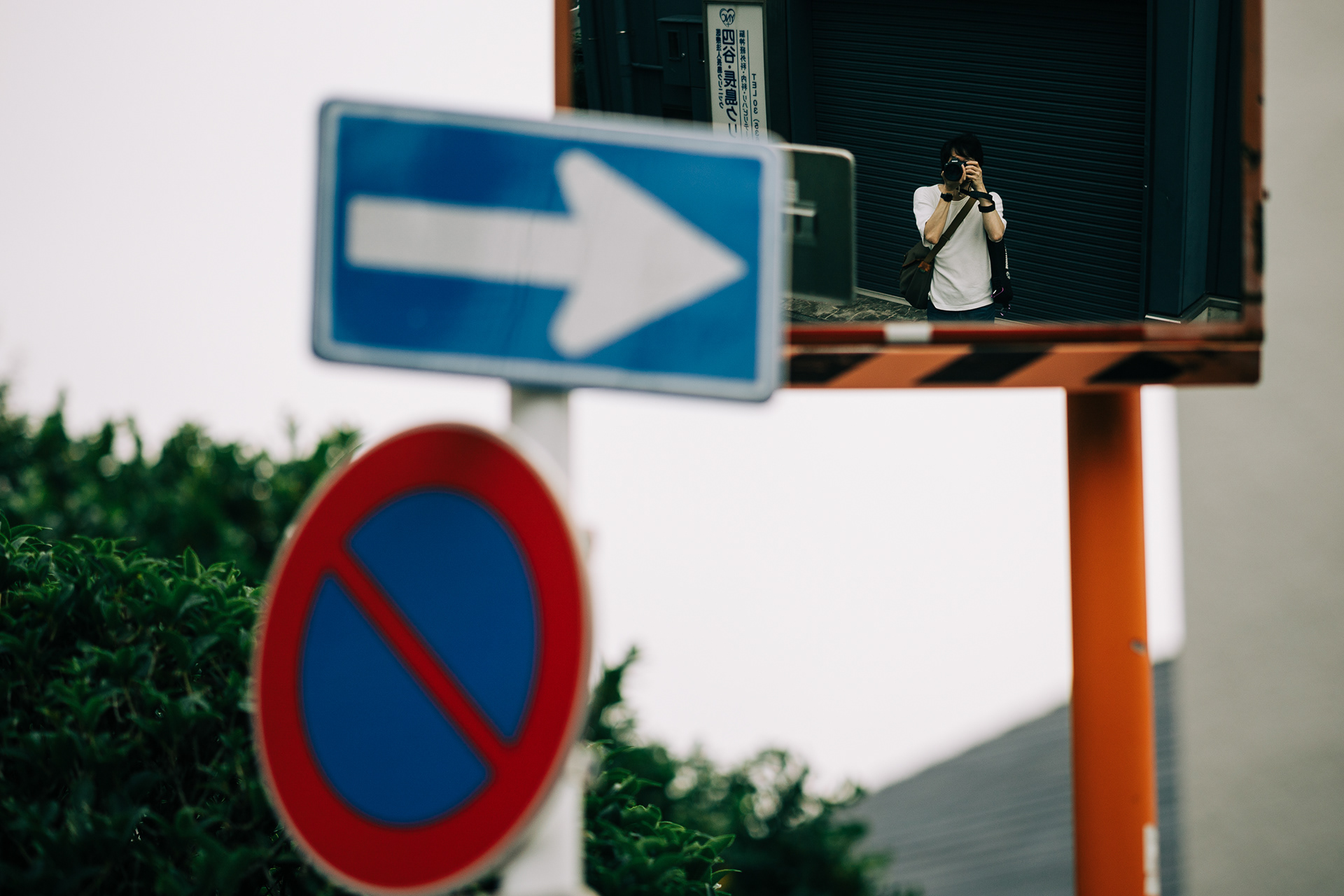 Fragmented urban perspective showing a photographer reflected in a convex street mirror amidst a labyrinth of Japanese directional signs and poles.
