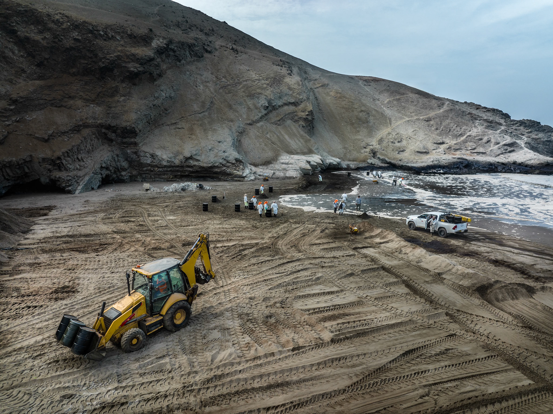 Aerial view of cleanup efforts after oil spill at "La Pampilla" refinery, Ancon, Lima, Peru on 2022. Workers in protective suits cleaning a sand beach on the shoreline.