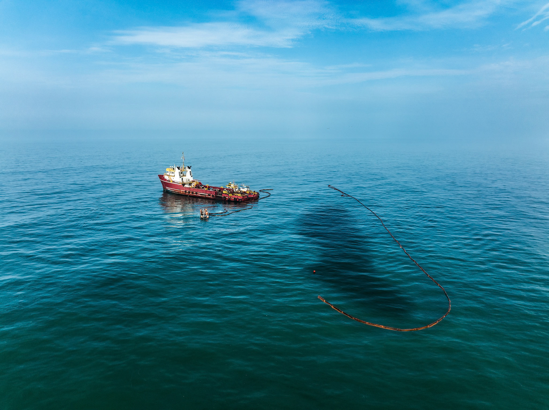 A ship works to contain an oil spill in the ocean, deploying barriers and equipment to mitigate environmental damage.