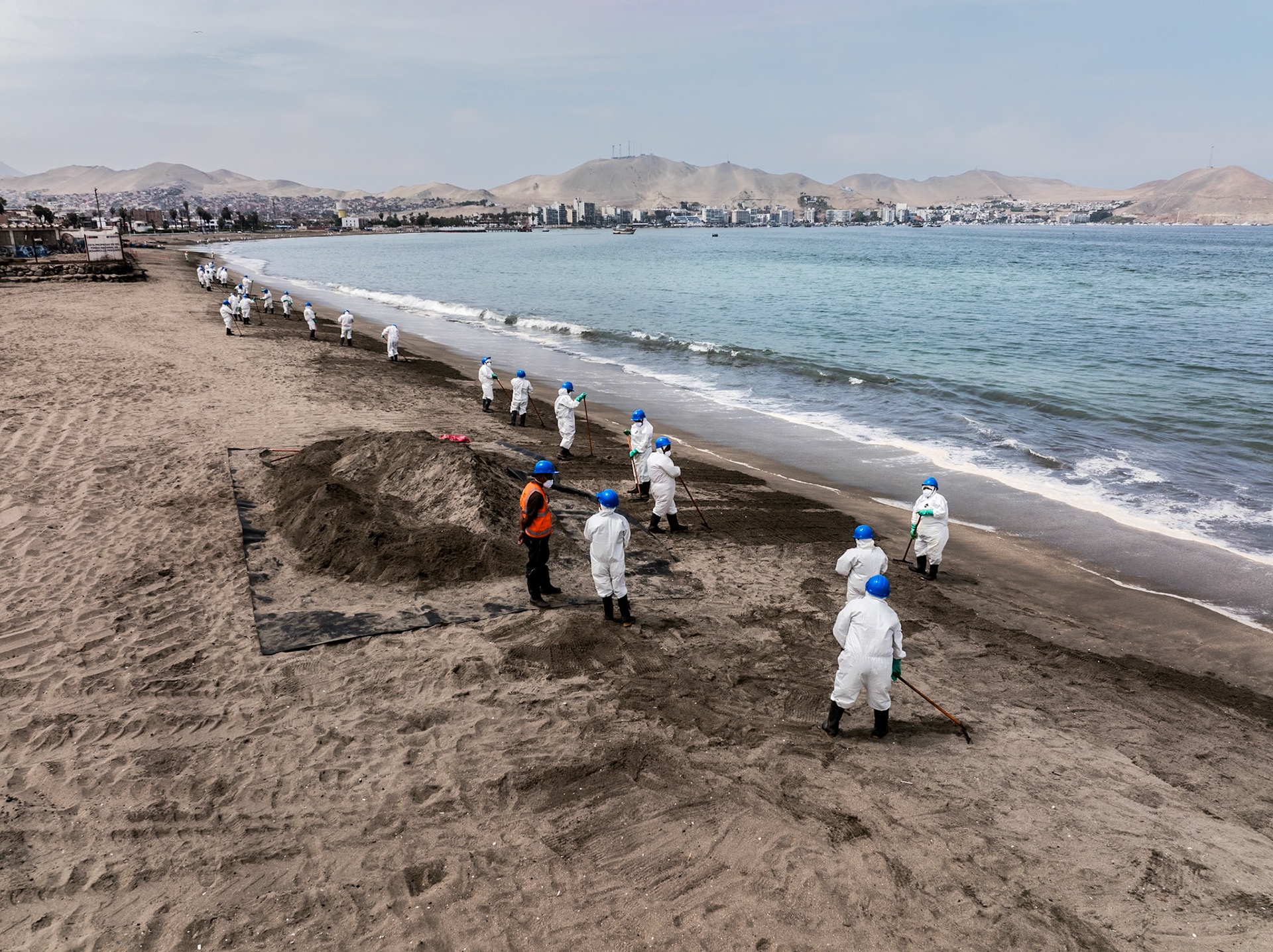 Aerial view of cleanup efforts after oil spill at "La Pampilla" refinery, Ancon, Lima, Peru on 2022. Workers in protective suits cleaning a sand beach on the shoreline.