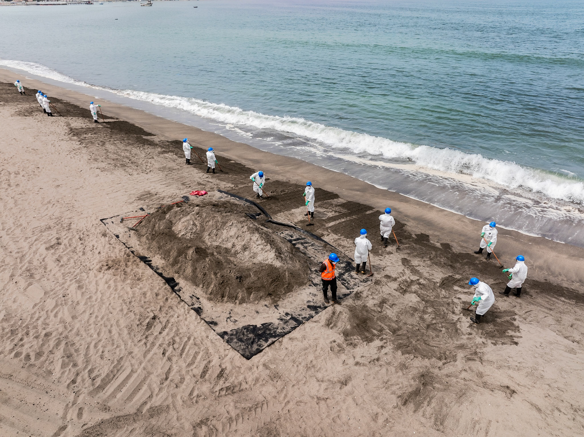 Aerial view of cleanup efforts after oil spill at "La Pampilla" refinery, Ancon, Lima, Peru on 2022. Workers in protective suits cleaning a sand beach on the shoreline.