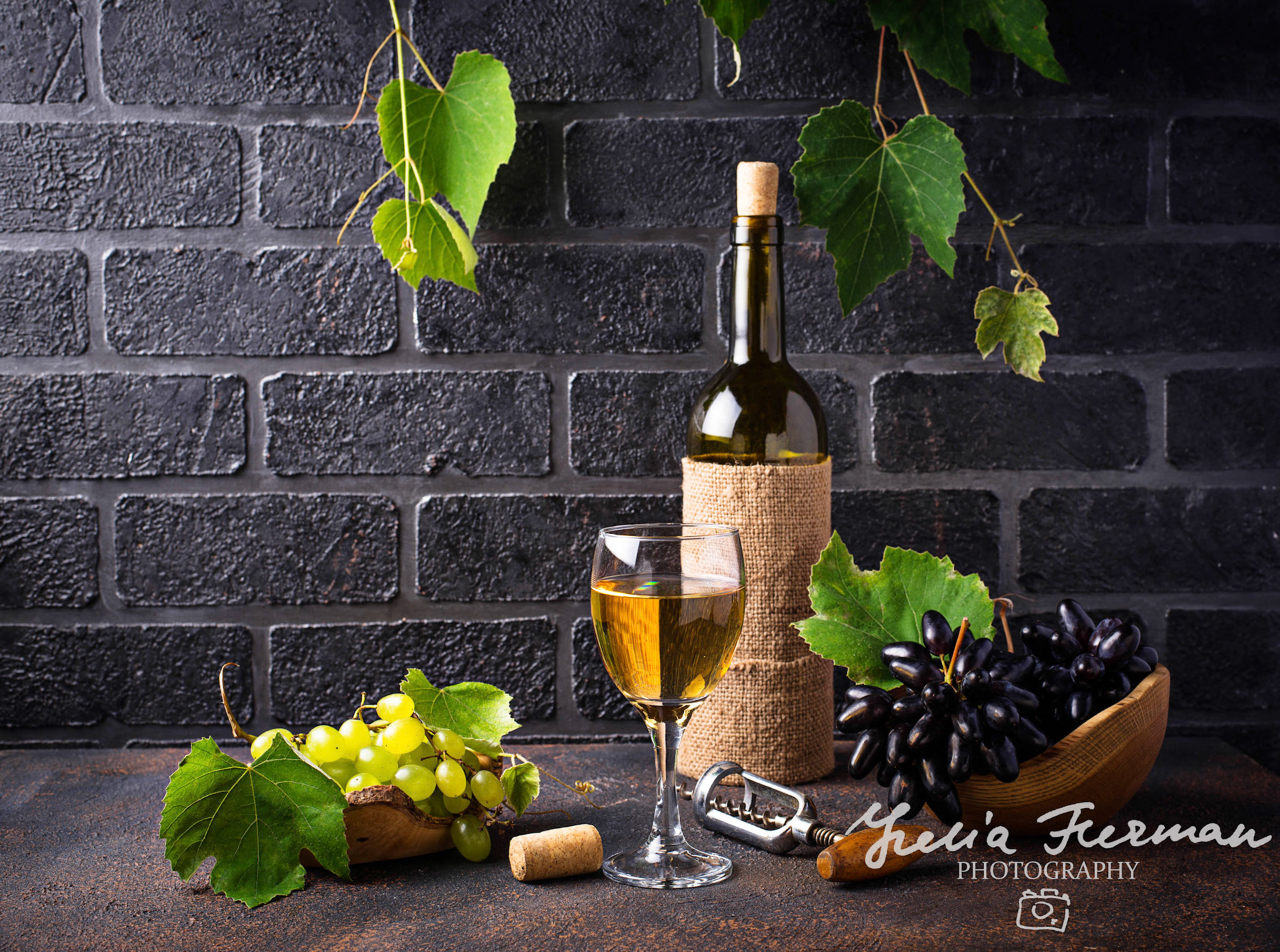 Grape, bottle and glass of white wine on brick wall