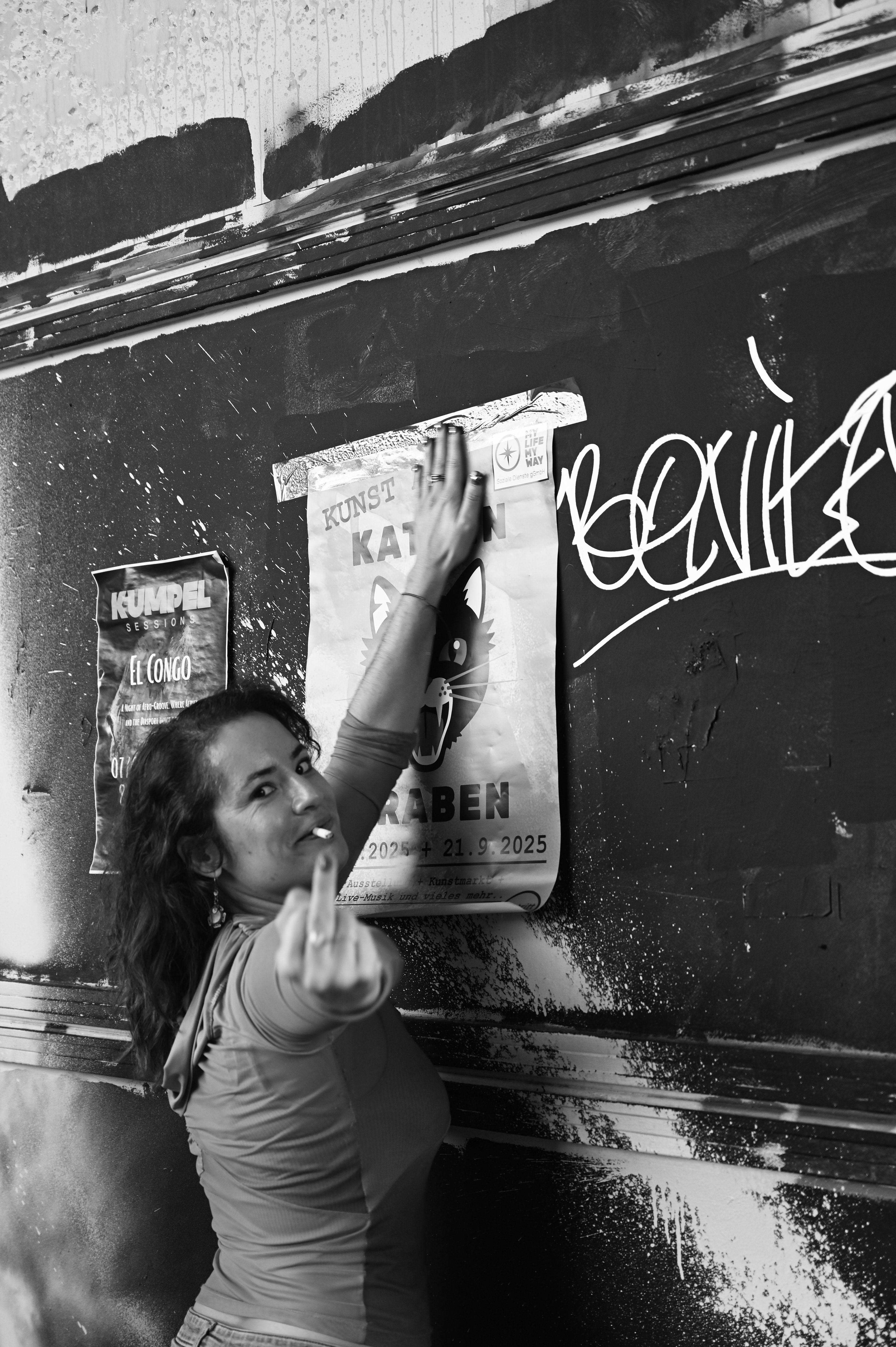 Künstlerin Dayra Palacios beim aufhängen des KAK Plakates, zeigt den Mittelfinger