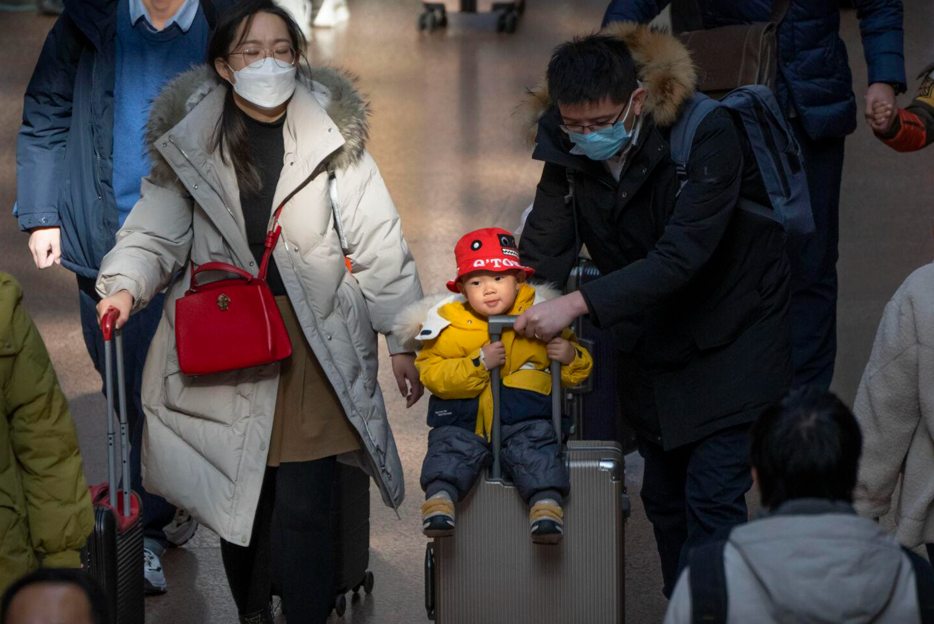 A man pushes a child riding on a suitcase at Beijing West Railway Station in Beijing, Wednesday, Jan. 18, 2023. A population that has crested and is slowly shrinking will pose new challenges for China's leaders, ranging from encouraging young people to start families, to persuading seniors to stay in the workforce longer and parents to allow their children to join the military. (Mark Schiefelbein/The Associated Press)