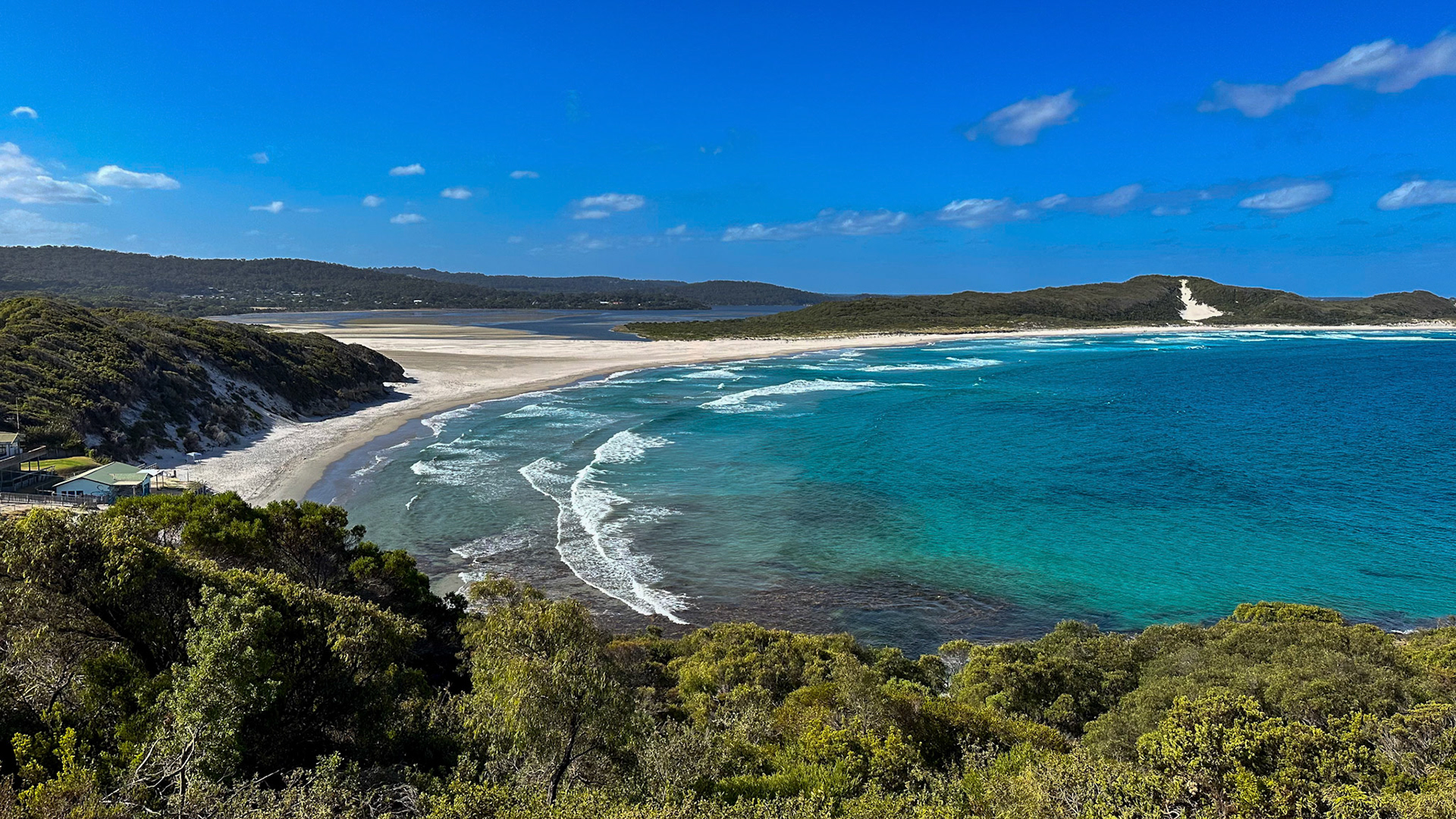 A panoramic view showcases a serene beach with turquoise waters, gentle waves, and lush foliage, evoking tranquility and natural beauty.