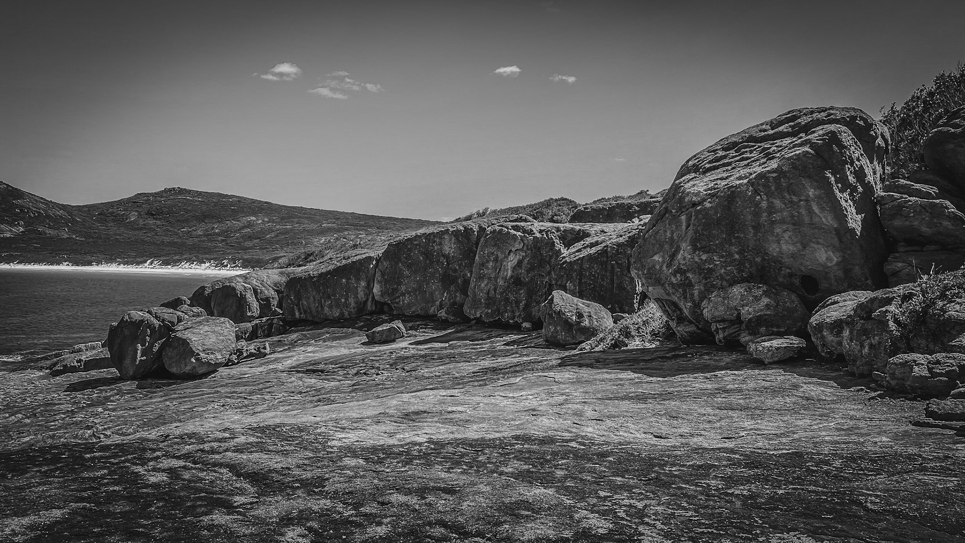 A striking black and white seascape showcases a rugged coastline, weathered rocks, and a serene ocean under a clear sky.