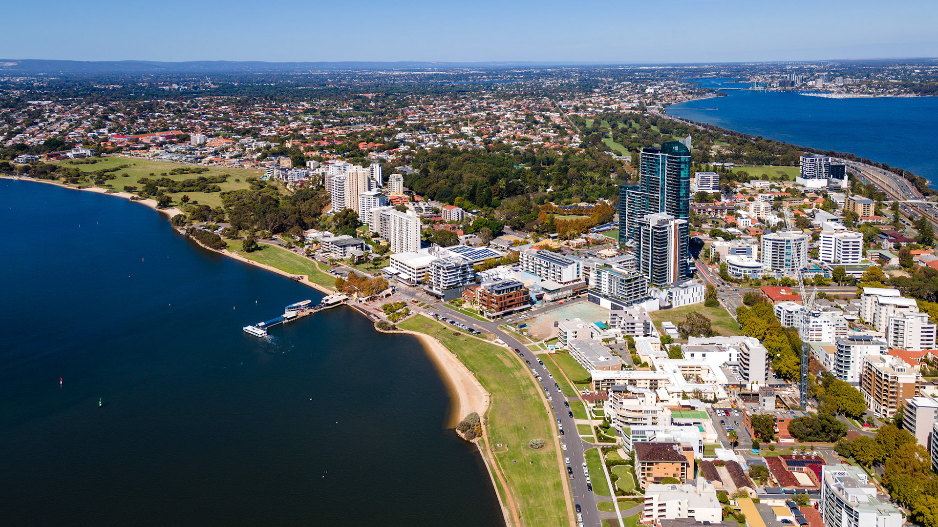 This breathtaking aerial scene showcases a lively riverside city filled with tall buildings nestled among green parks.