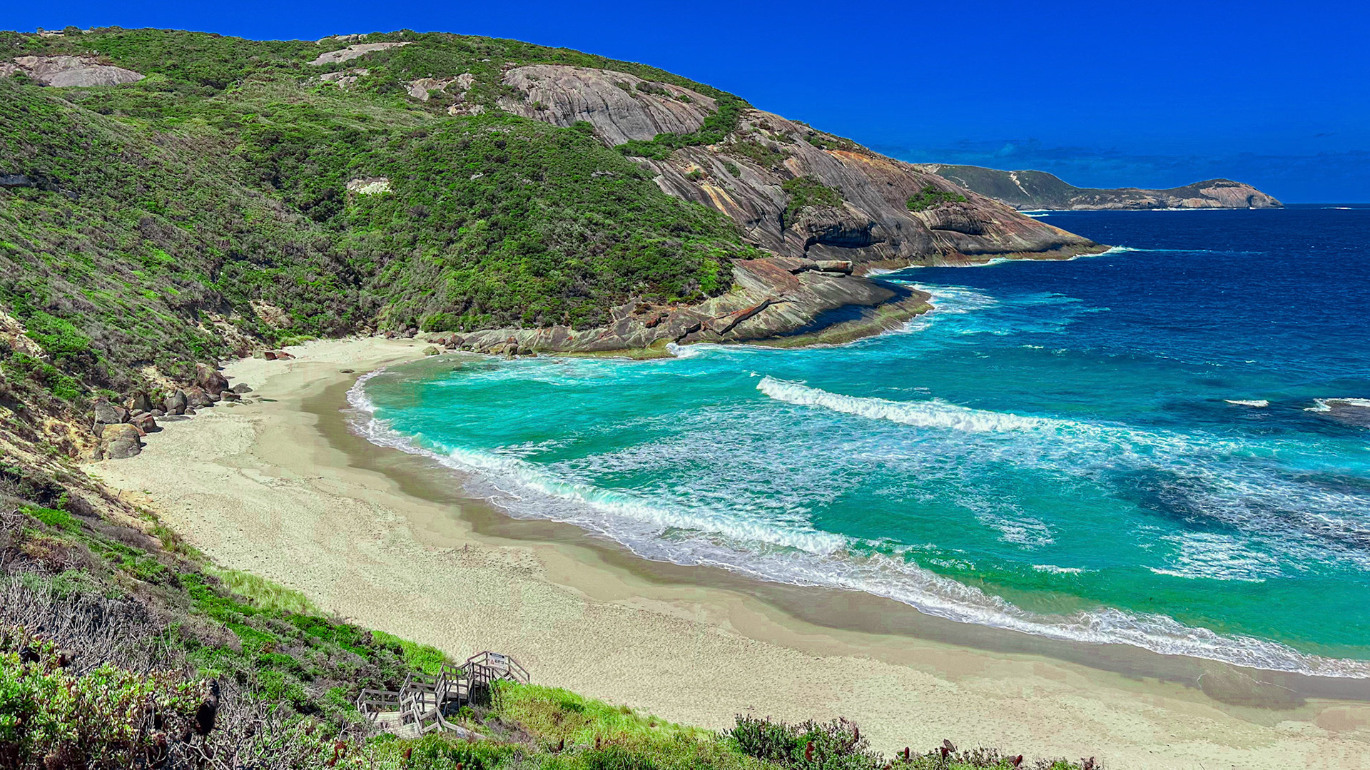 A tranquil beach scene features crashing waves, lush hills, and vibrant ocean waters, evoking a sense of natural beauty and escape.