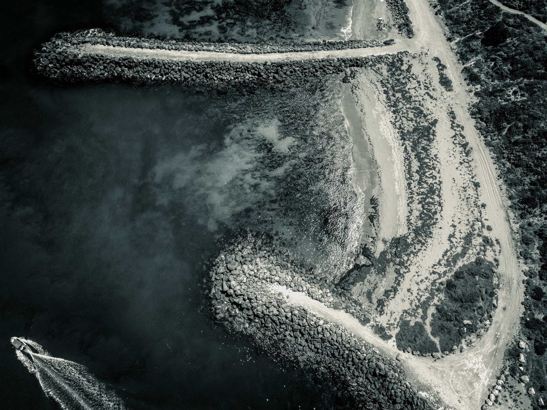 An aerial view showcases a coastal landscape with a breakwater, boat, and shoreline. The scene reflects movement and isolation.