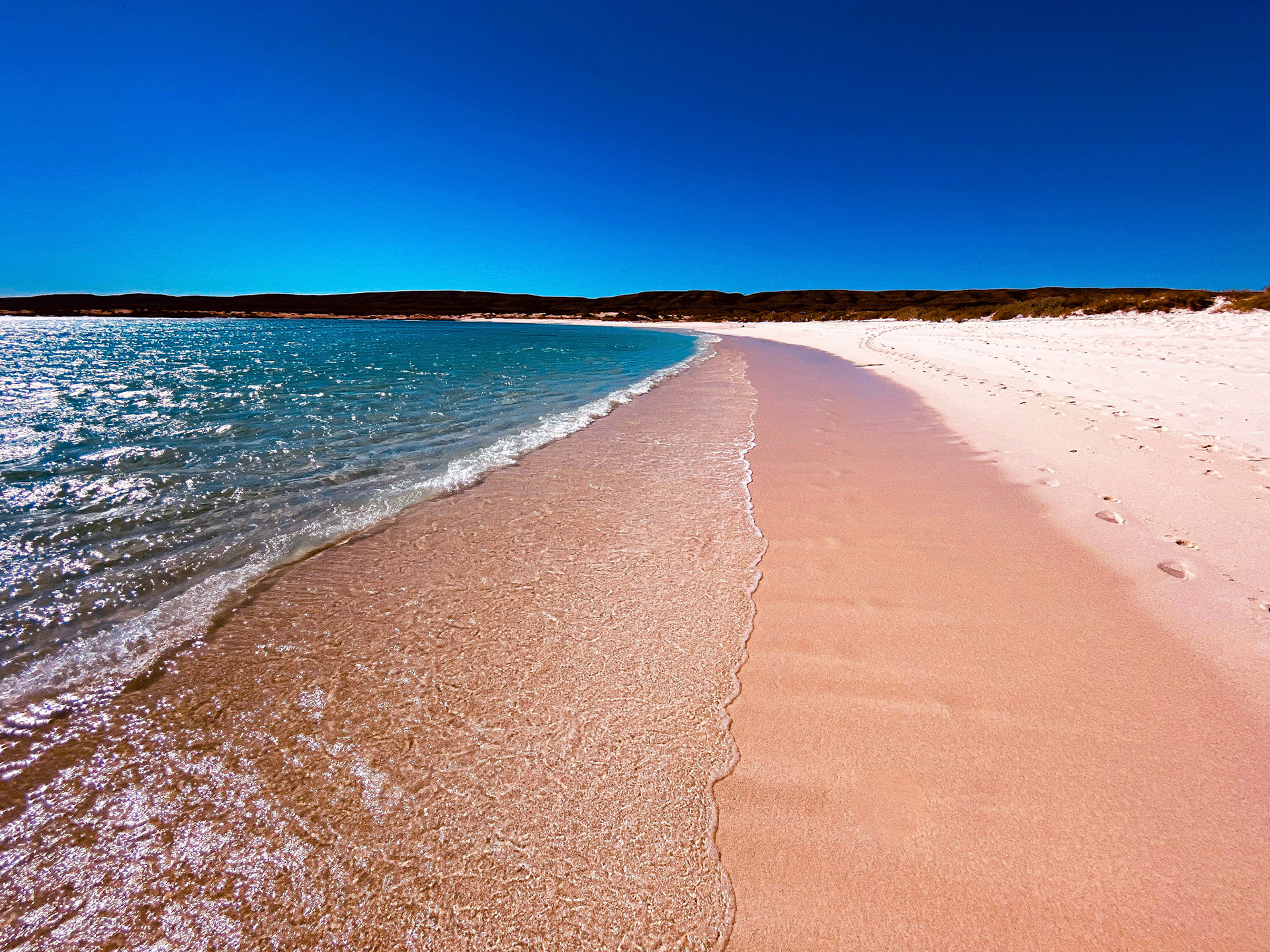 A tranquil beach scene features soft pink sand, gentle waves, and clear turquoise water, evoking feelings of paradise and relaxation.
