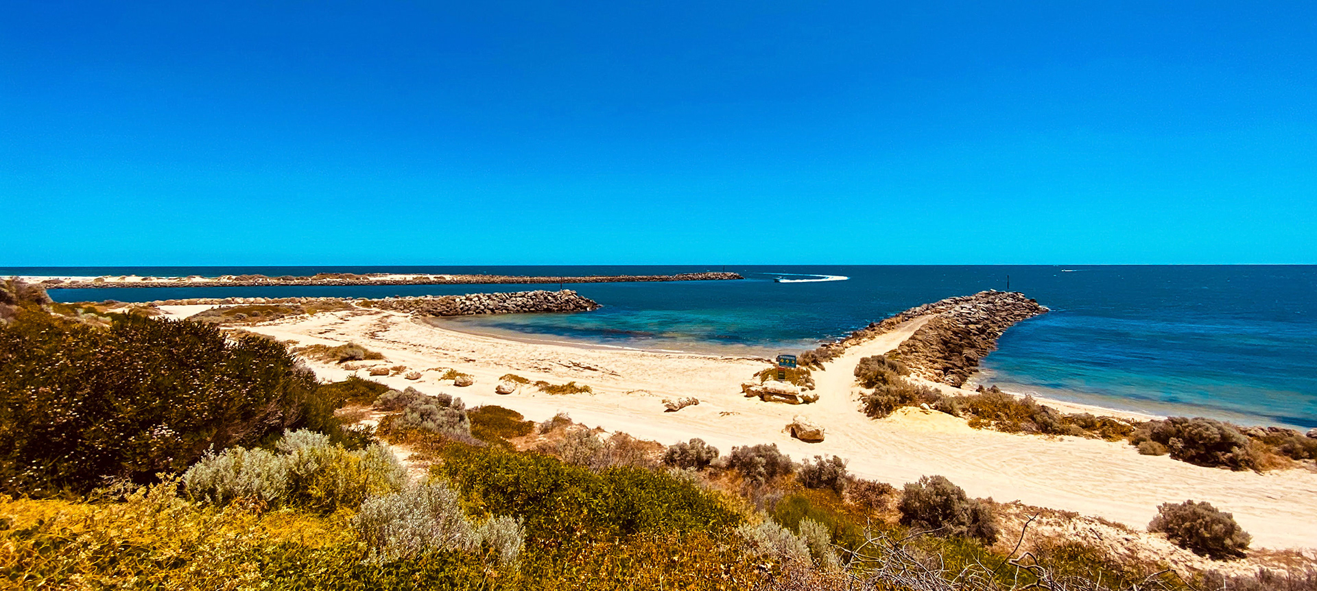 A panoramic view showcases a tranquil coastal landscape with a sandy beach, calm ocean, and clear blue sky, evoking serenity.