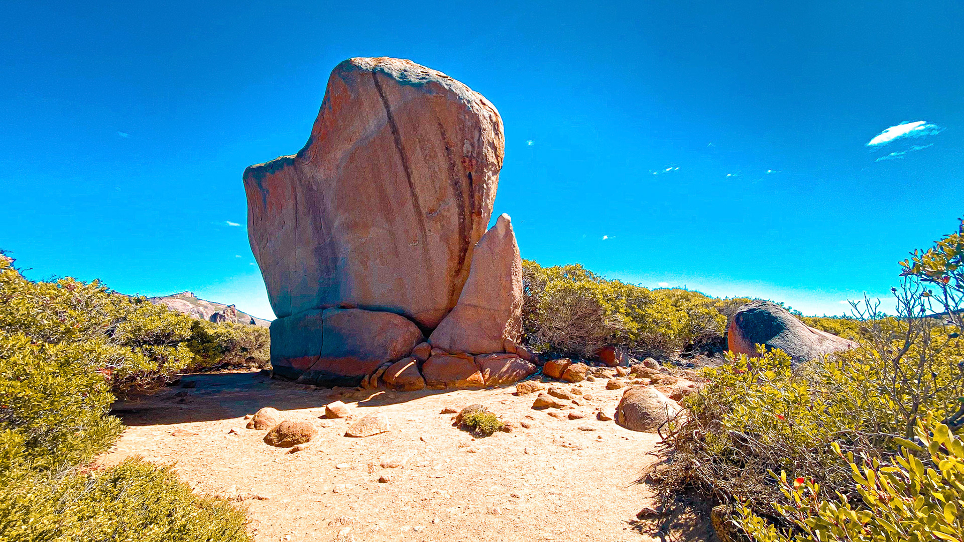 A massive rock formation stands in a dry landscape, showcasing timelessness and geological wonder under a clear blue sky.