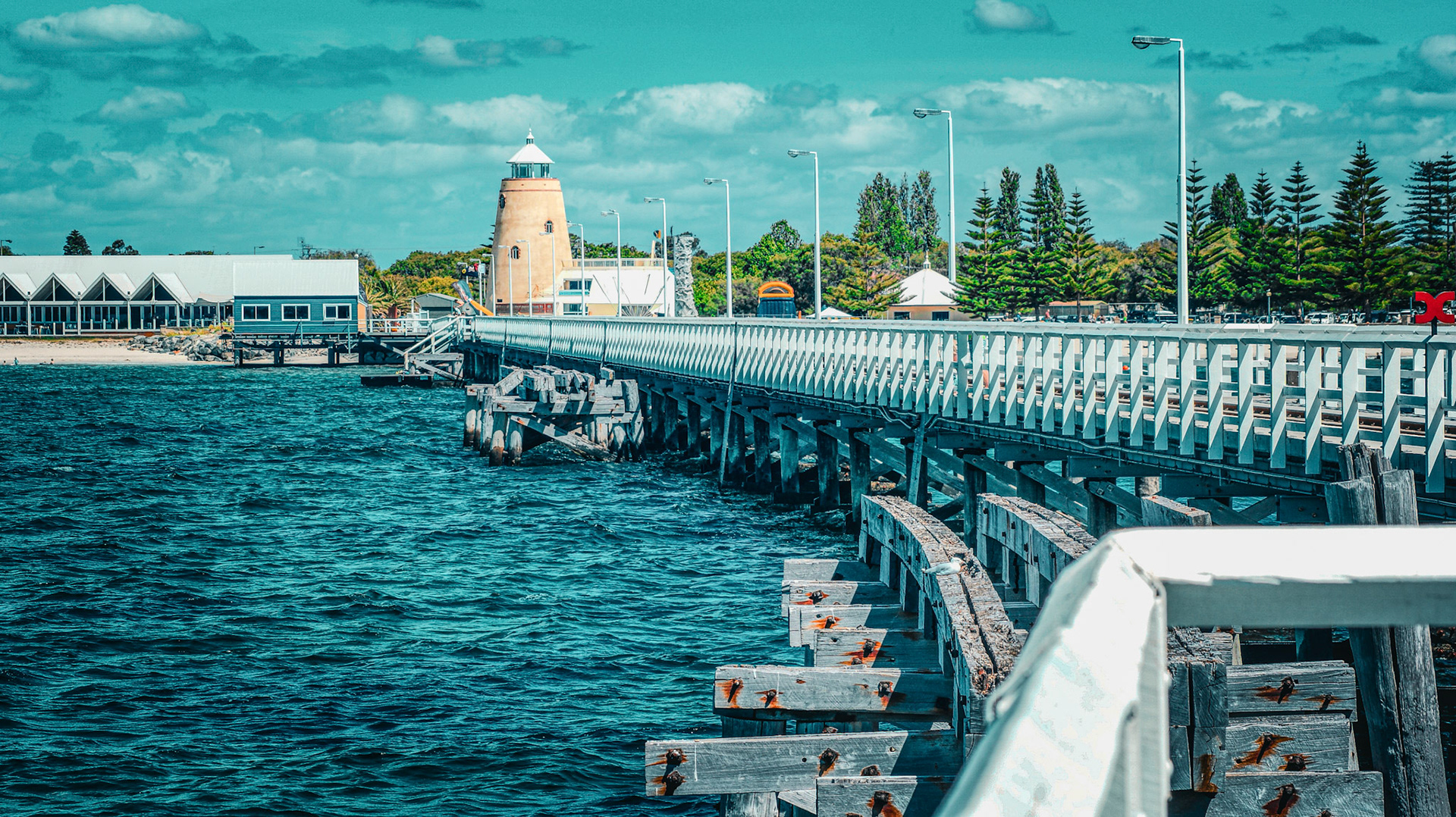 A long, weathered wooden pier extends into a vibrant ocean, showcasing coastal charm and tranquility under a partly cloudy sky.