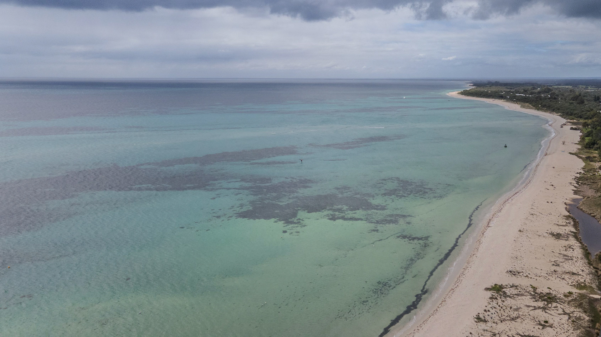 An expansive aerial view of a tranquil coastline featuring clear turquoise waters and a sandy beach. The image captures the natural beauty of the coast, stretching into the horizon with scattered cloud cover adding depth to the atmosphere. This serene coastal landscape offers a perfect blend of oceanic hues and sandy textures, ideal for conveying a sense of peace and relaxation.