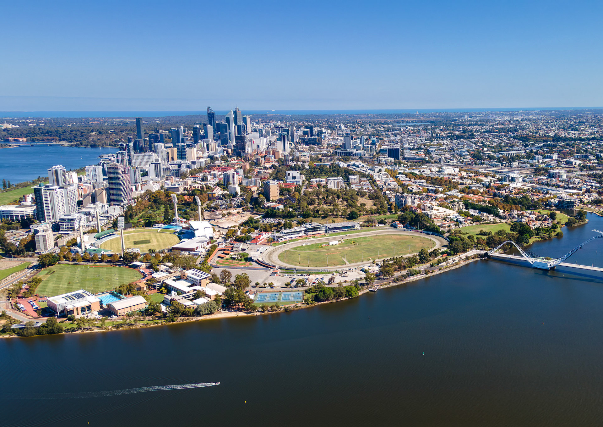 Vibrant cityscape of Perth showcases modern architecture alongside the serene waters of the Swan River. Green parks and bustling city life thrive under a brilliant blue sky.
