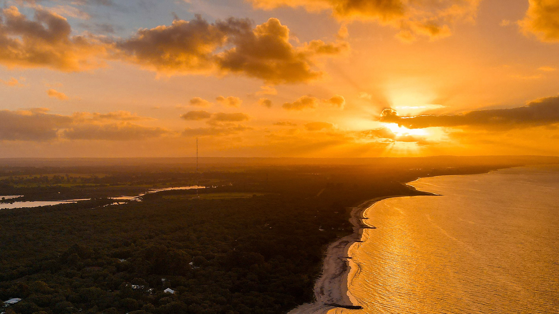 A breathtaking aerial view of a stunning coastal landscape during sunset, featuring golden hues reflecting on the water and a scenic horizon of clouds. The contrasting textures of the land and sea create a serene and inspiring natural scene, perfect for themes related to tranquility, nature, and beauty.