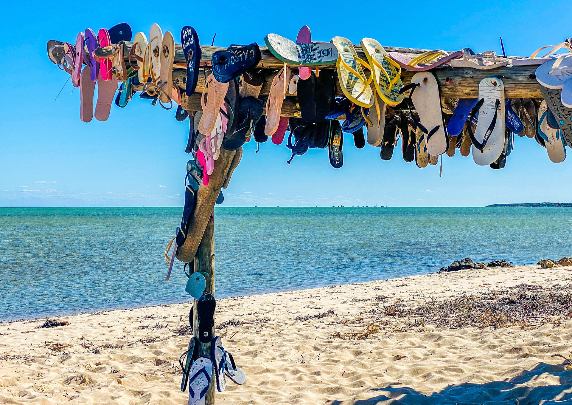 A vibrant collection of flip-flops hangs from a wooden structure on the beach, evoking summer nostalgia and carefree leisure.