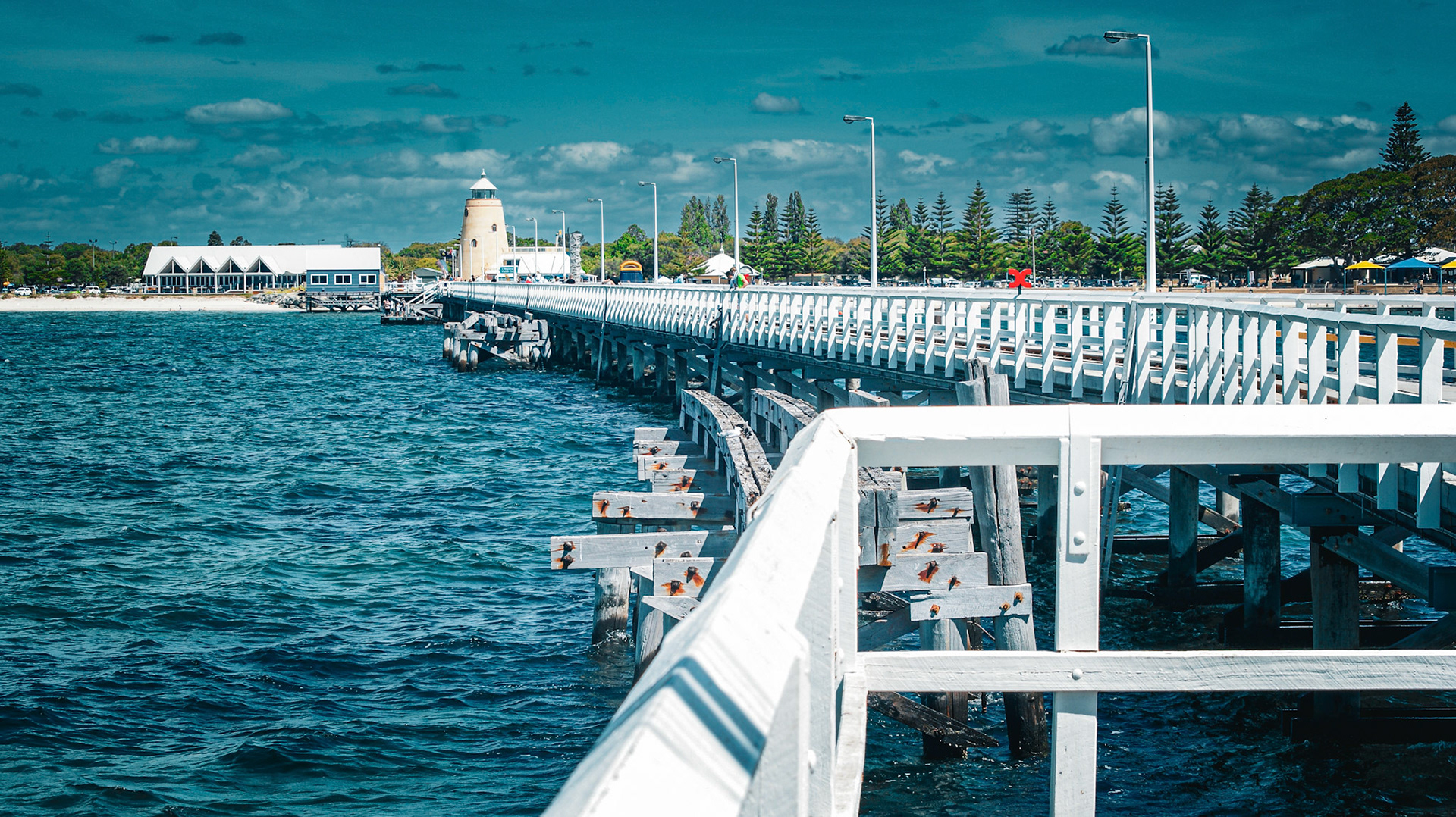 A long white wooden pier extends into the ocean, featuring a lighthouse at its end. This serene coastal scene embodies travel and exploration.