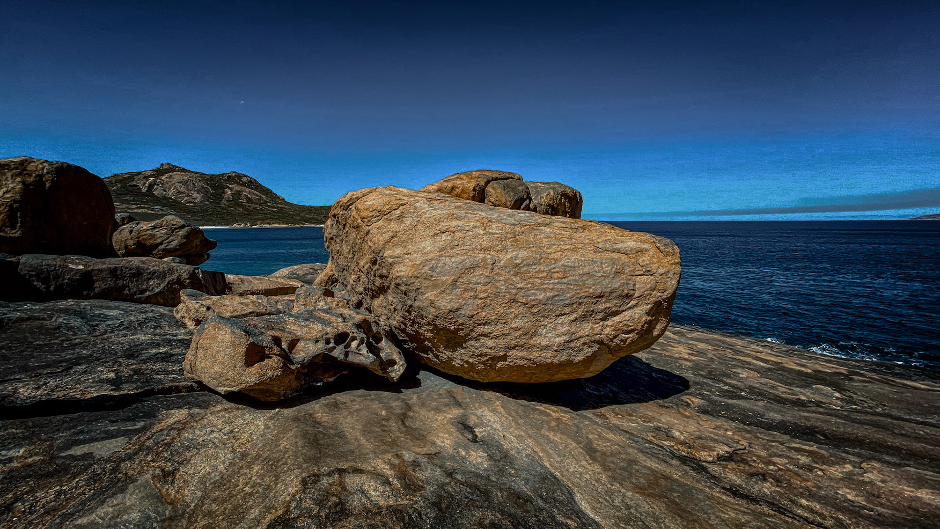 A low-angle perspective reveals weathered granite boulders along a rocky coastline, showcasing the ocean's vastness and natural beauty.