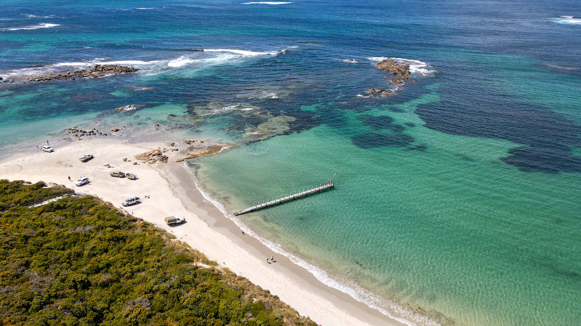 Explore a tranquil coastal landscape featuring a sandy beach, turquoise waters, and a wooden pier, perfect for a peaceful getaway.