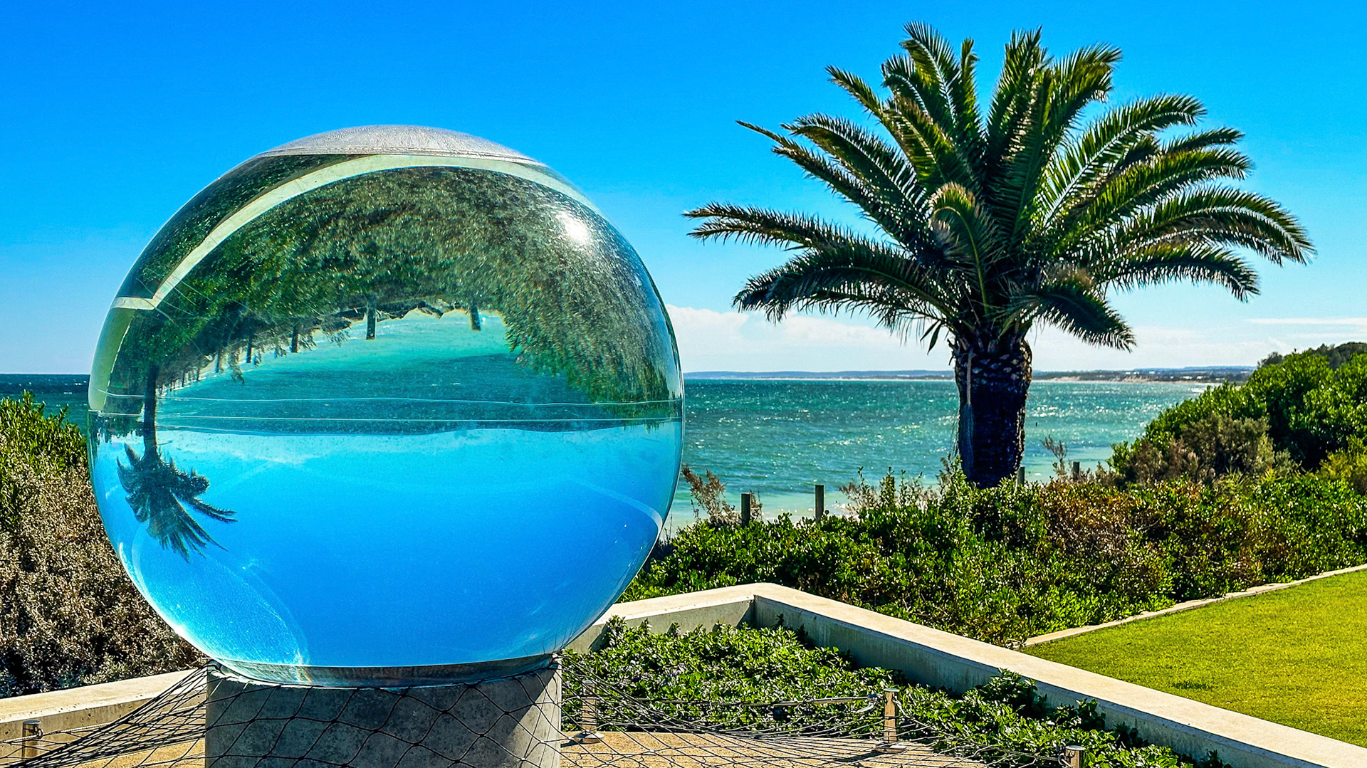 A glass sphere captures a serene tropical landscape, reflecting palm trees and the ocean, evoking a sense of calm and clarity.