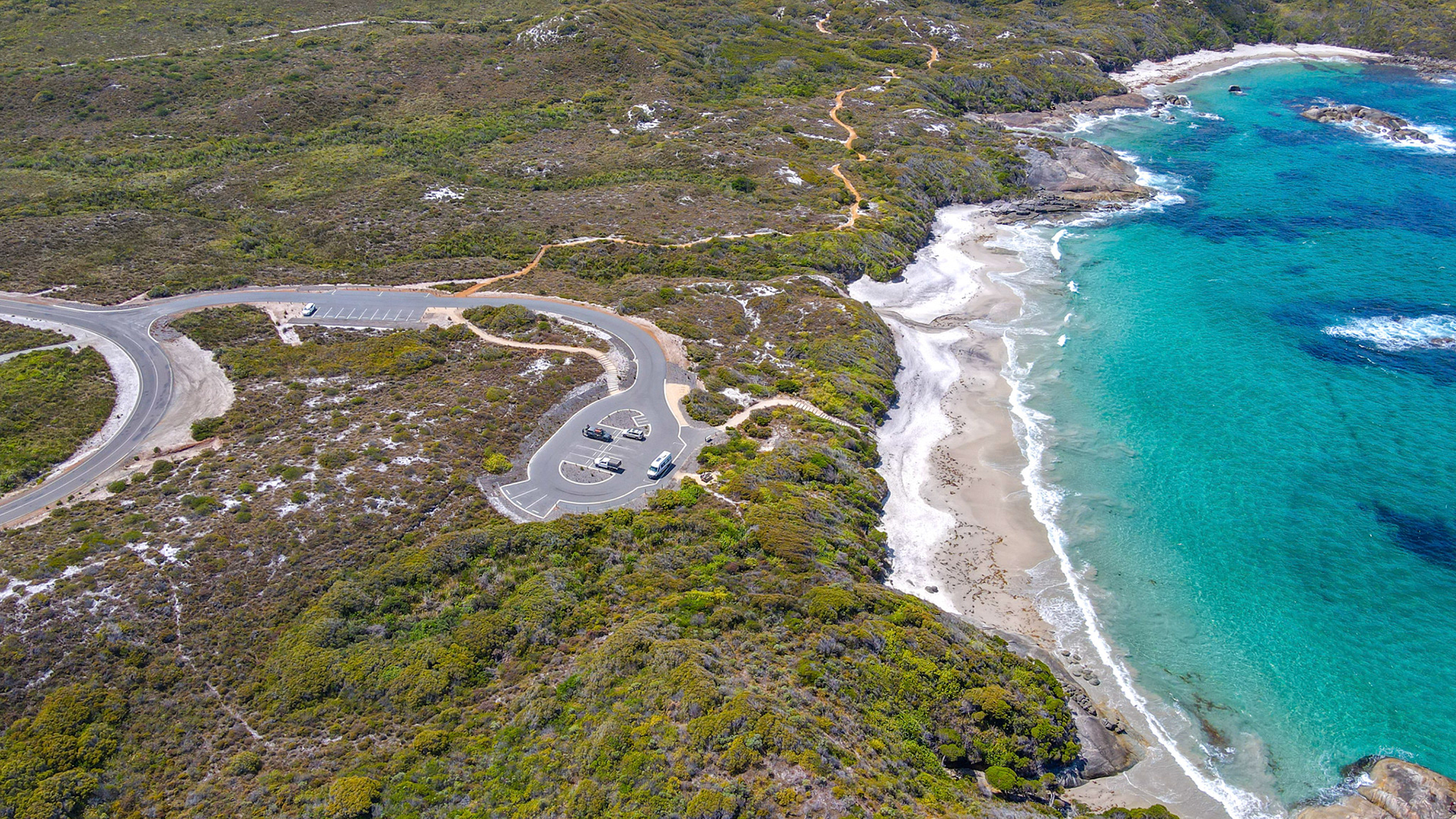 Discover a breathtaking coastline featuring a serene beach, winding road, and vibrant nature, perfect for outdoor recreation.