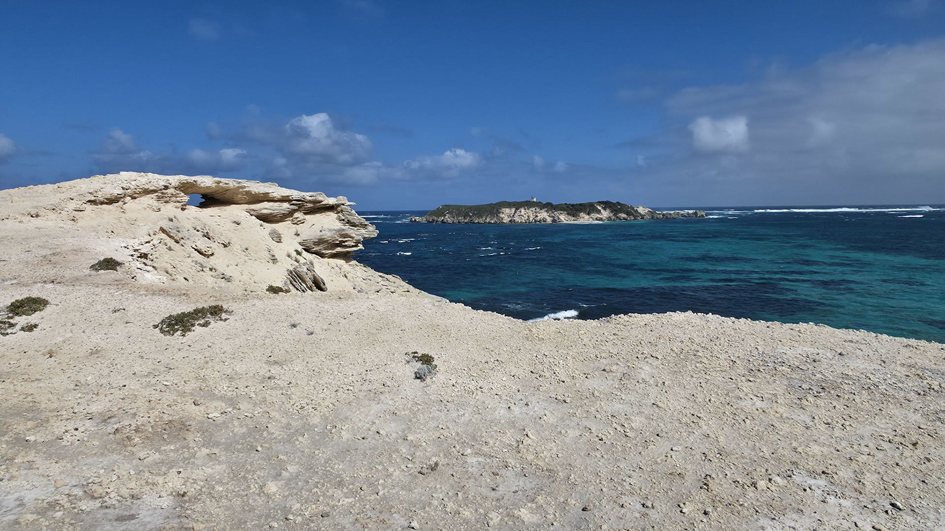 A breathtaking view of a rugged coastal rock formation under a clear blue sky. The pristine turquoise waters of the ocean contrast beautifully with the textured limestone cliffs, creating a serene and picturesque landscape. This image captures the essence of natural beauty and the tranquility of a remote shoreline.