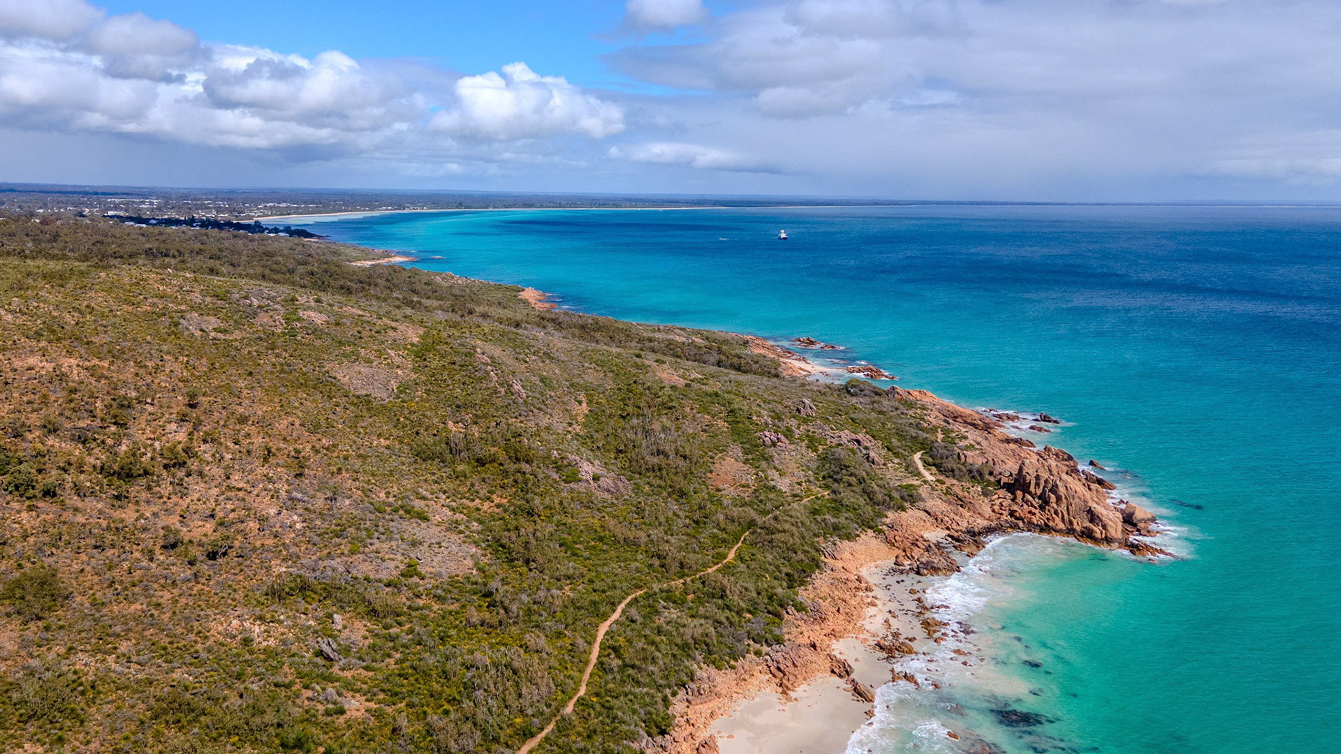 An expansive aerial view showcasing a beautiful coastal landscape. The image captures the stunning contrast between the turquoise ocean and the rugged coastline covered with lush greenery. Intermittent sandy beaches and rocky outcrops add texture to the vista, under a partly cloudy sky that stretches to the horizon. This tranquil scene epitomizes natural beauty, perfect for travel inspiration or environmental themes.