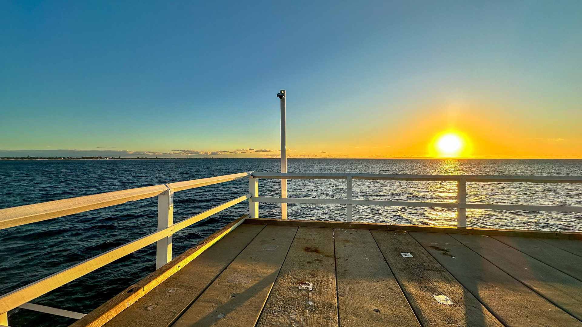 A vibrant sunset over the ocean from a wooden pier reflects tranquility and peace. The warm glow captures nature's beauty.