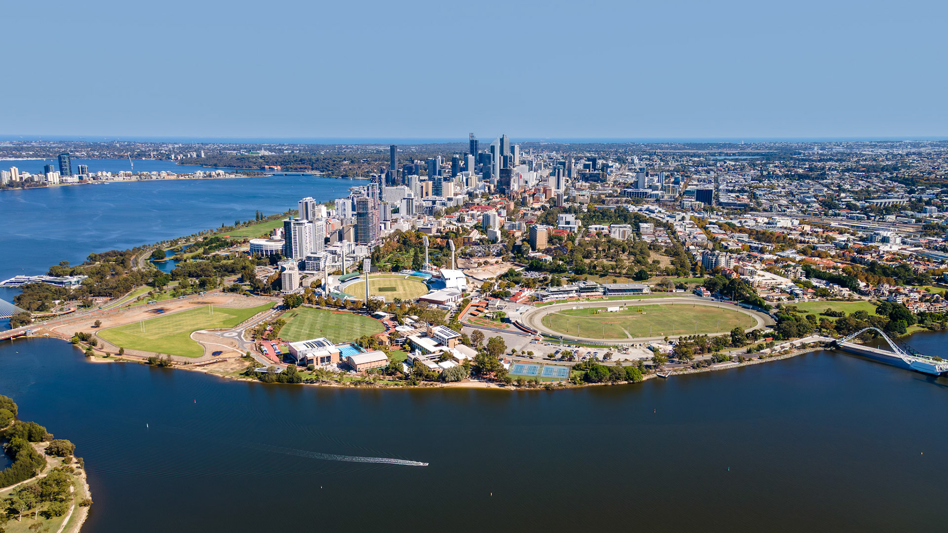 Vibrant green parks and sparkling waters create a captivating contrast with the gleaming skyscrapers of Perth. This scene captures a lively urban oasis under a clear blue sky in late spring.