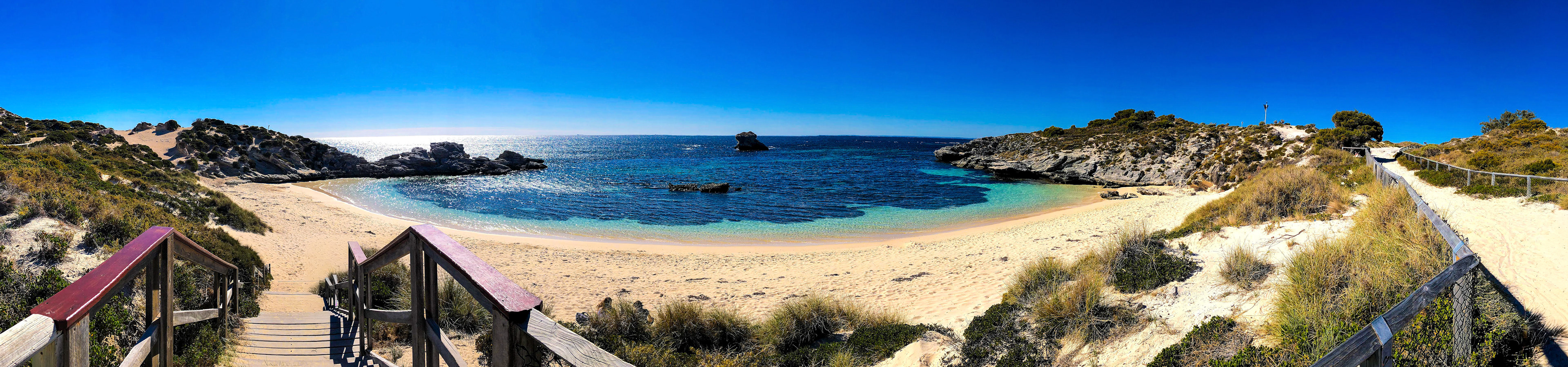 A panoramic view showcases a tranquil beach with golden sand, turquoise waters, and a clear blue sky, inviting exploration.