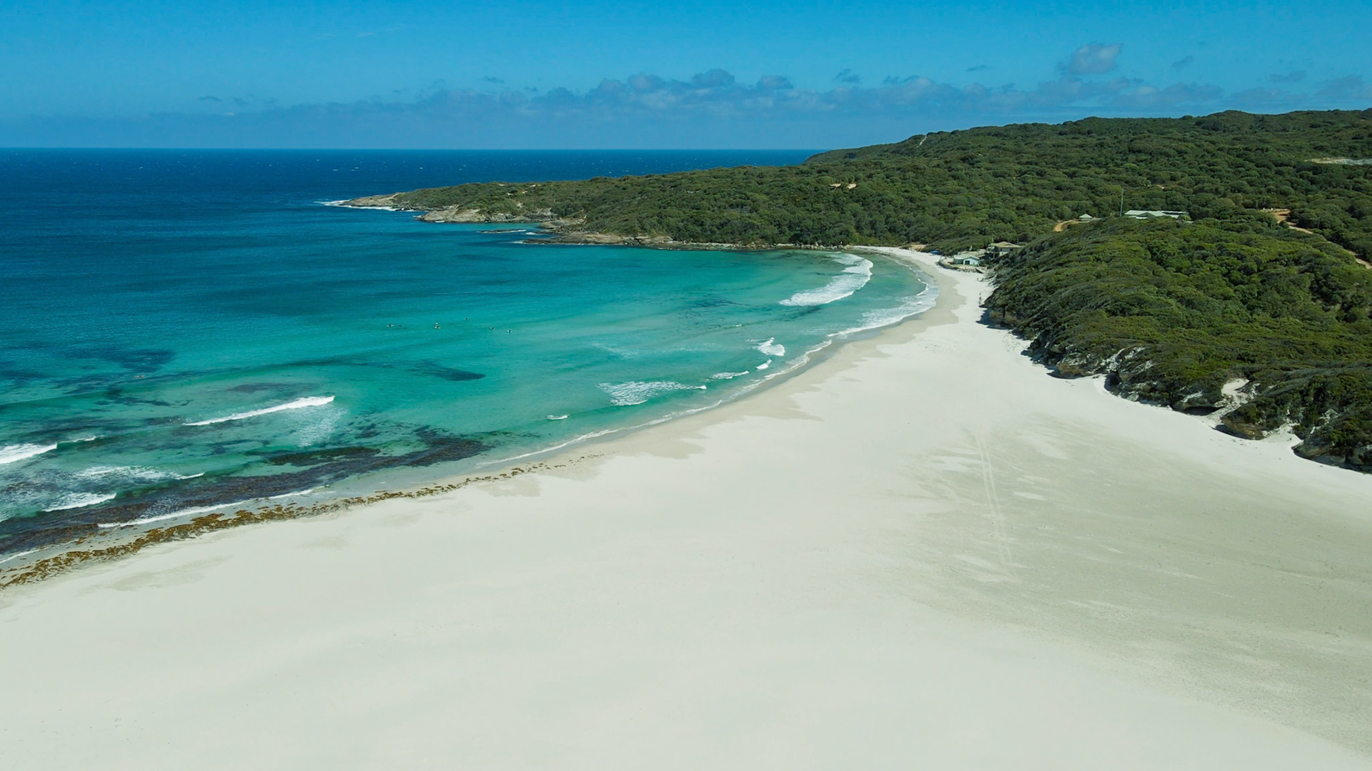 Experience the serenity of a pristine beach with turquoise waters, gentle waves, and lush hills, perfect for a tranquil escape.