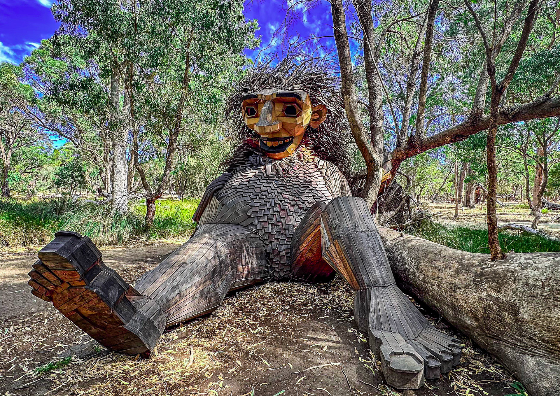 A whimsical giant troll wooden sculpture sits in a sunlit forest clearing, showcasing creativity and fantasy in nature.
