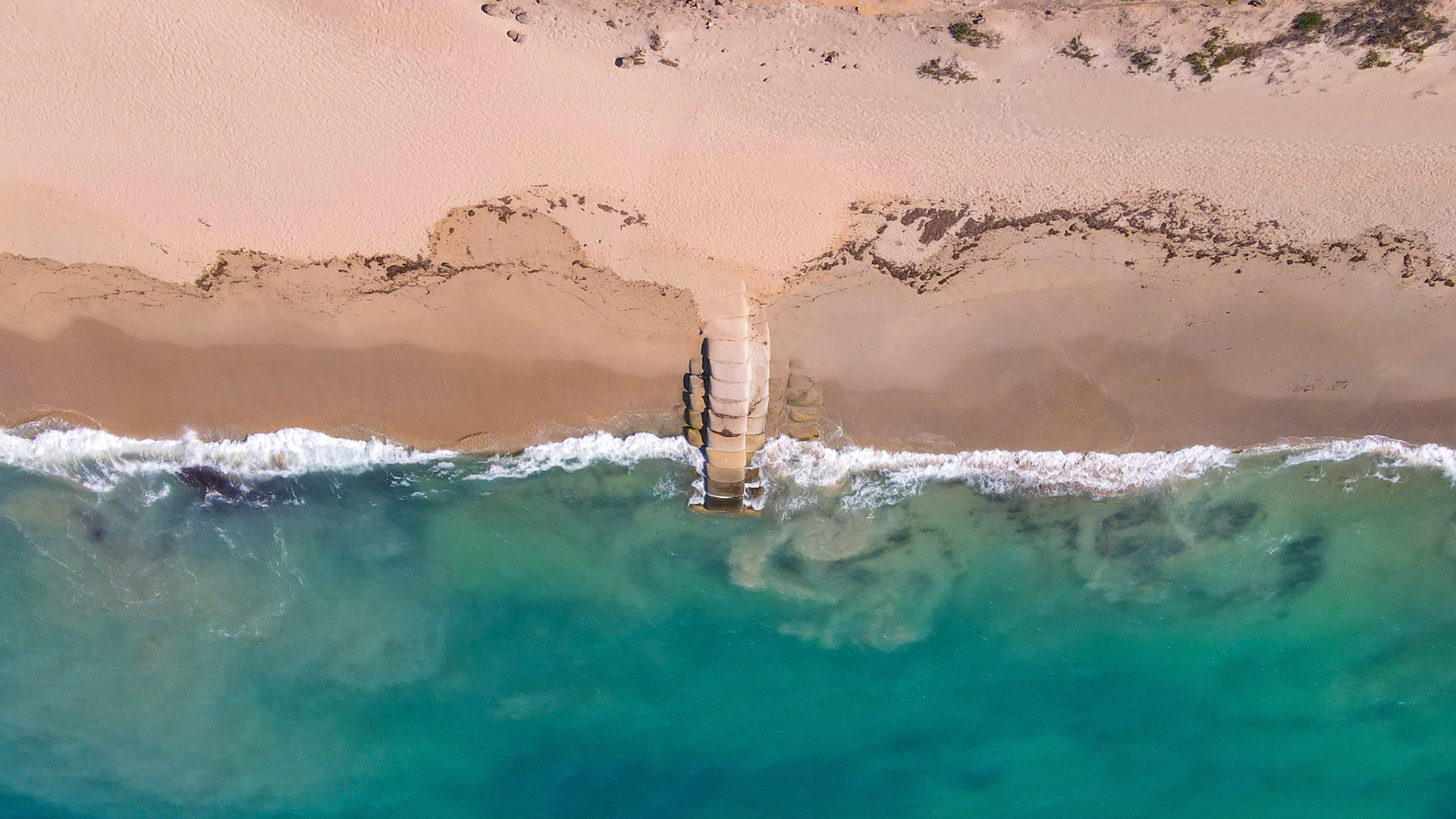 An aerial view showcases a tranquil beach where gentle waves meet the ocean. The scene highlights the beauty of nature and coastal landscapes.