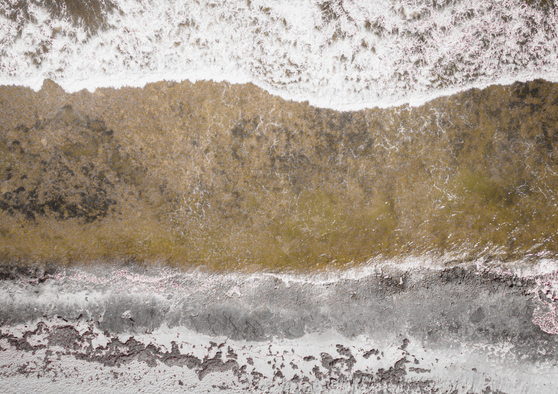 An abstract aerial view shows ocean waves crashing against a textured shoreline, highlighting nature's powerful forces.