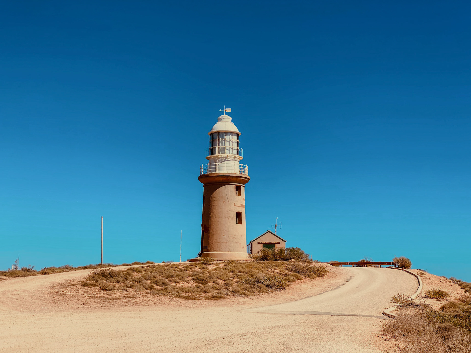 A solitary lighthouse stands on a windswept hill, a beacon for maritime navigation under a clear blue sky.