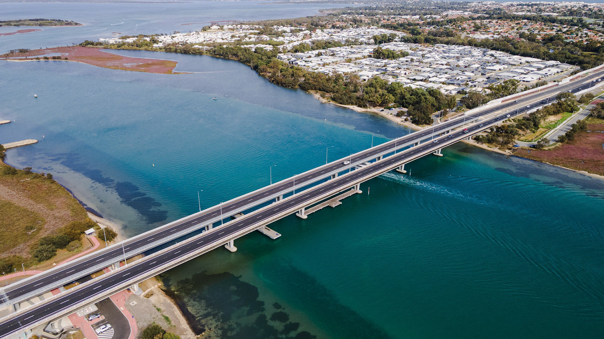 Stunning aerial shot showcasing a modern bridge connecting two coastal areas. The image captures the serenity of the turquoise water below, highlighting the lush greenery and residential areas nearby. Ideal for projects related to infrastructure, transportation, urban planning, and coastal environments. The vibrant colors of both the water and vegetation create an inviting visual that will enhance various media types, from promotional materials to educational content.